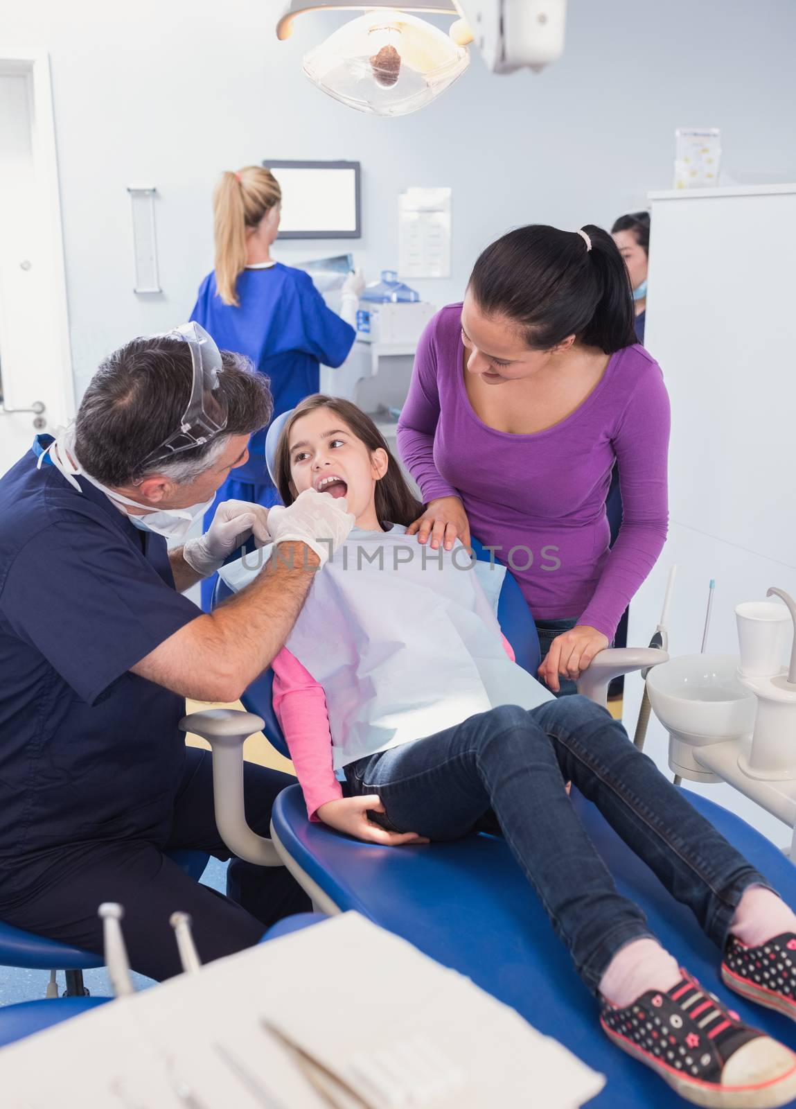 Pediatric dentist examining young patient with her mother in dental clinic
