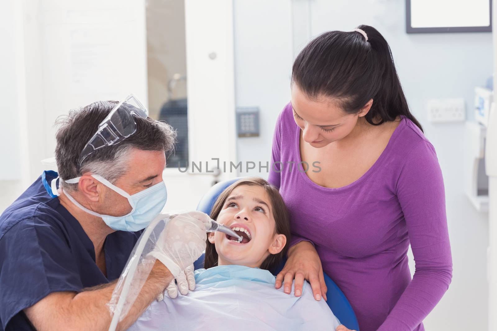 Pediatric dentist examining young patient with her mother in dental clinic