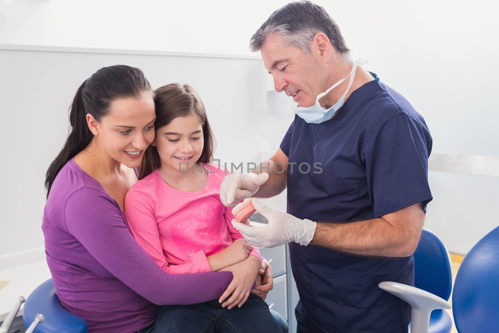 Pediatric dentist explaining to young patient and her mother the model in dental clinic