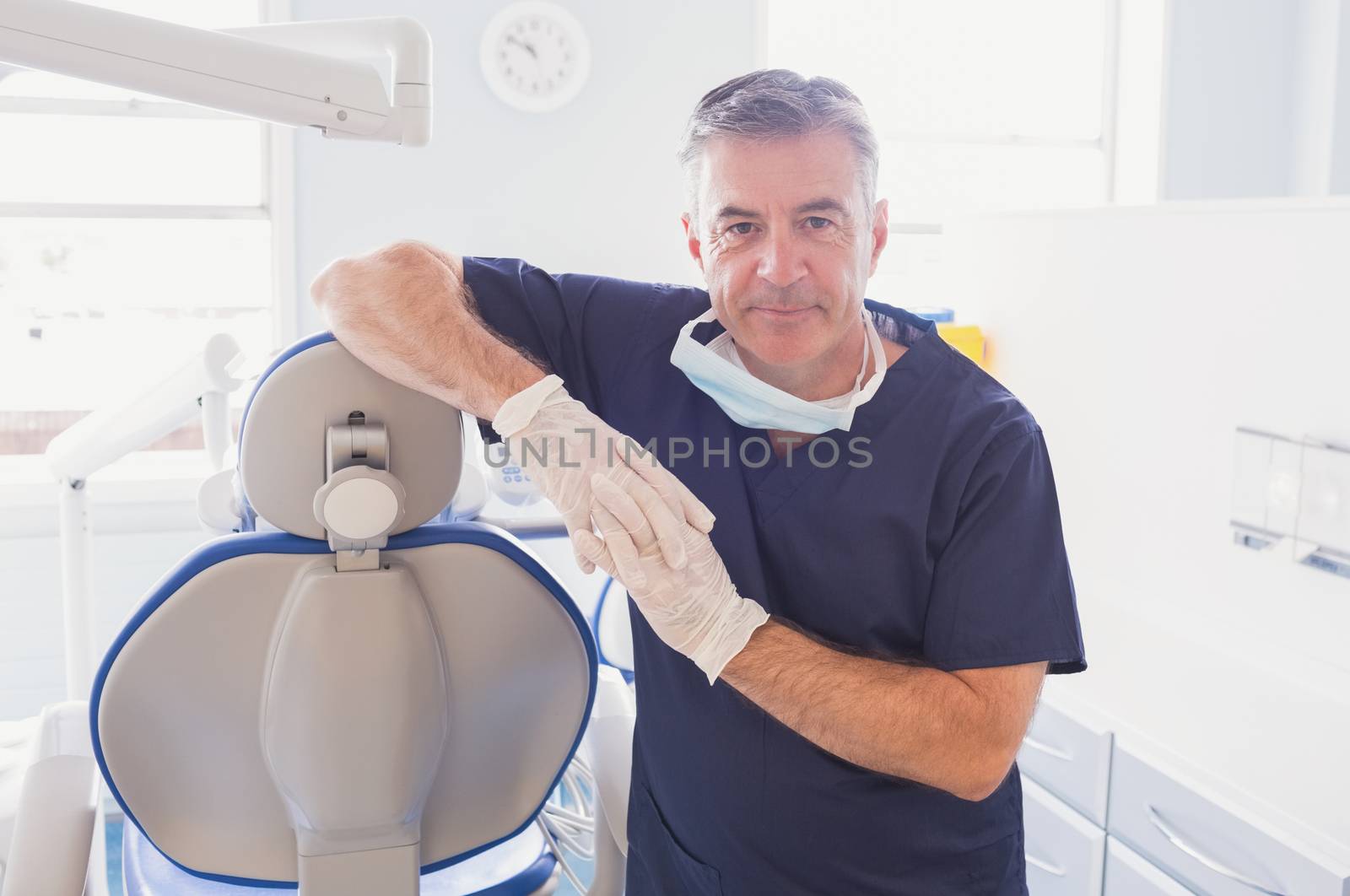 Smiling dentist leaning against dentists chair  by Wavebreakmedia