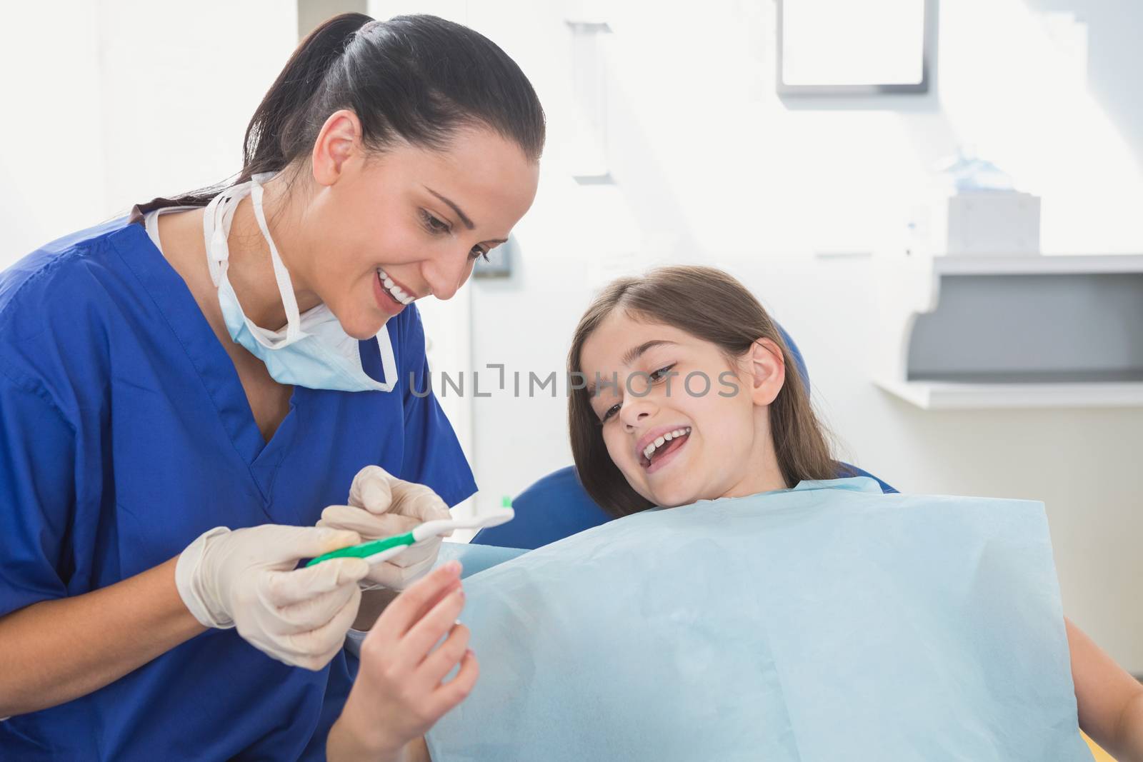 Smiling pediatric dentist explaining to young patient the toothbrush by Wavebreakmedia