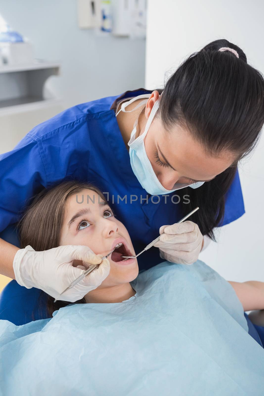 Pediatric dentist using dental explorer and angled mirror in mouth open of a patient 