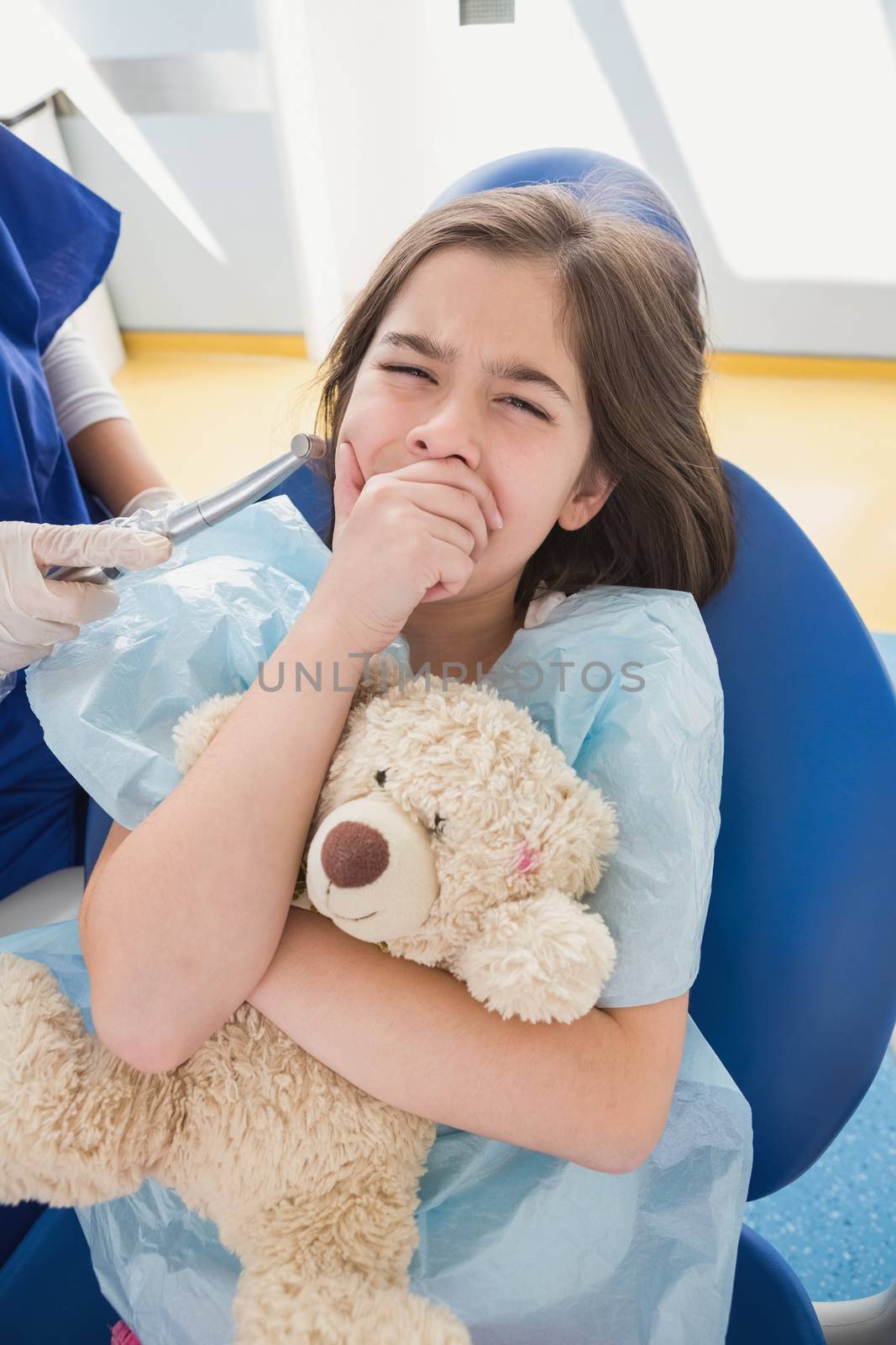 Scared patient covering mouth and holding teddy bear in dental clinic