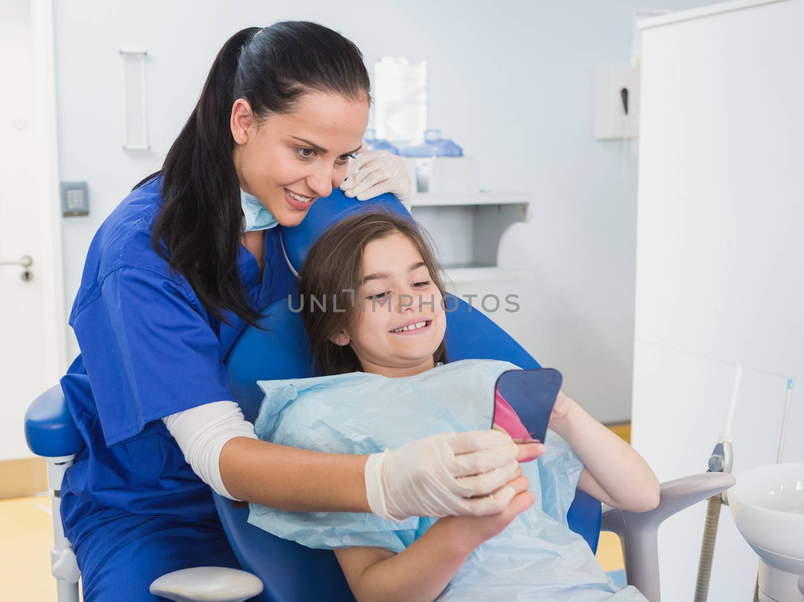 Pediatric dentist and young patient holding a mirror by Wavebreakmedia