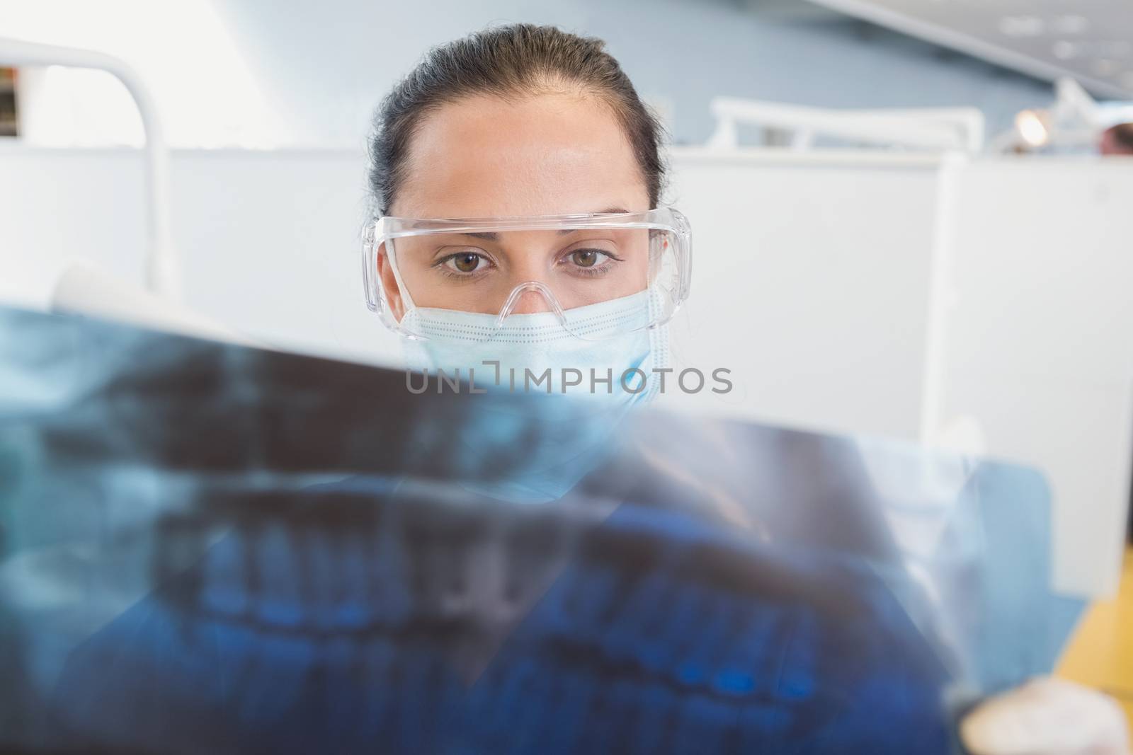 Dentist wearing surgical mask and safety glasses studying the x-ray