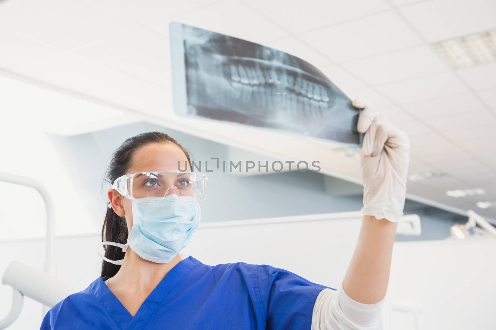 Dentist wearing surgical mask and safety glasses studying the x-ray