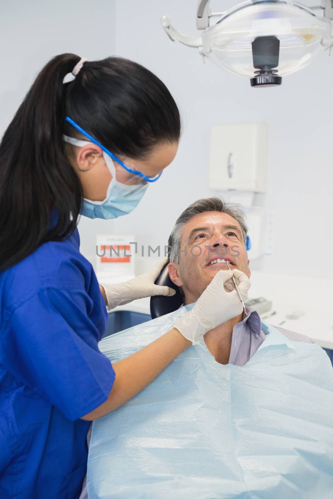 Dentist wearing surgical mask and safety glasses examining a patient 
