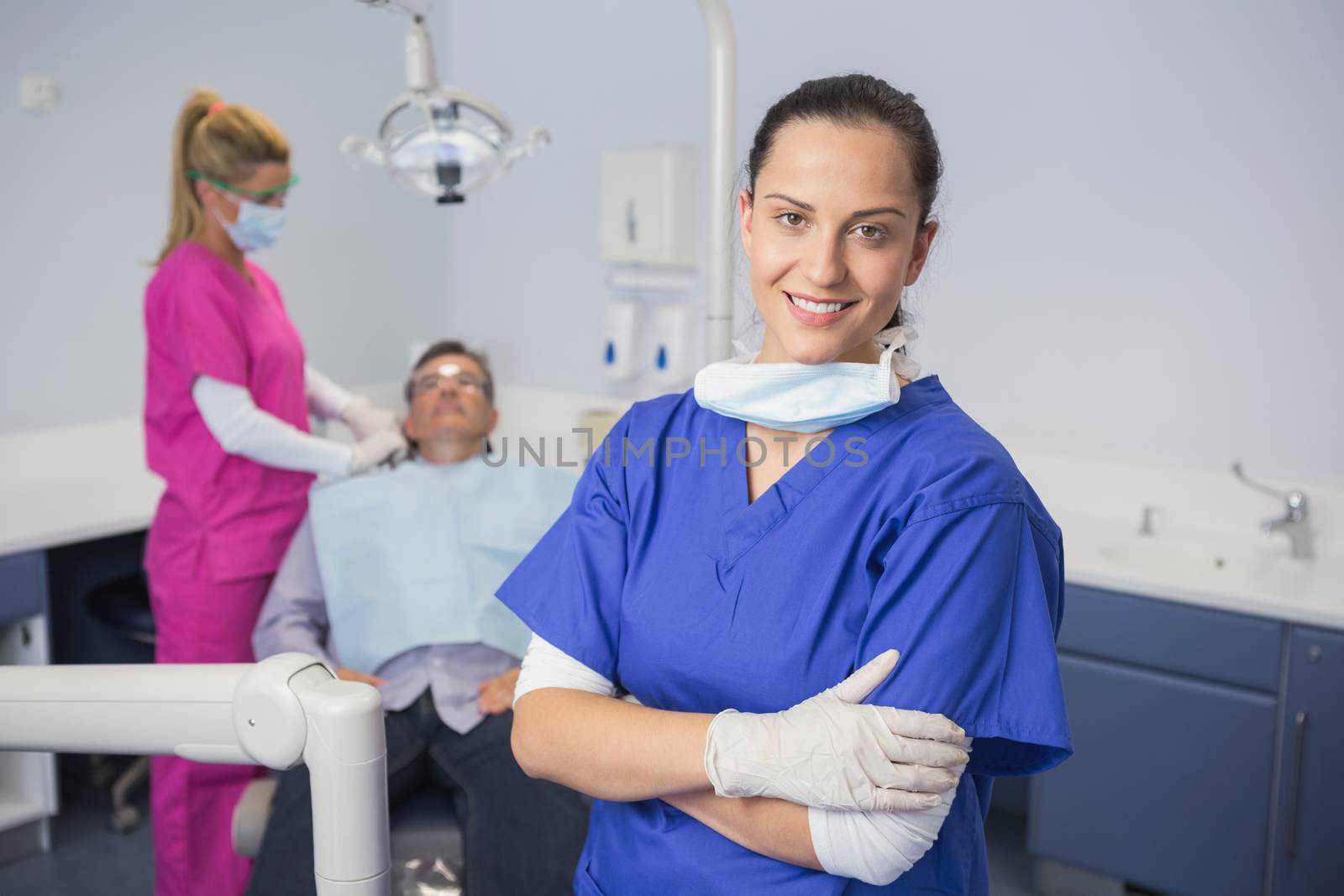Smiling dentist with arms crossed and patient behind her