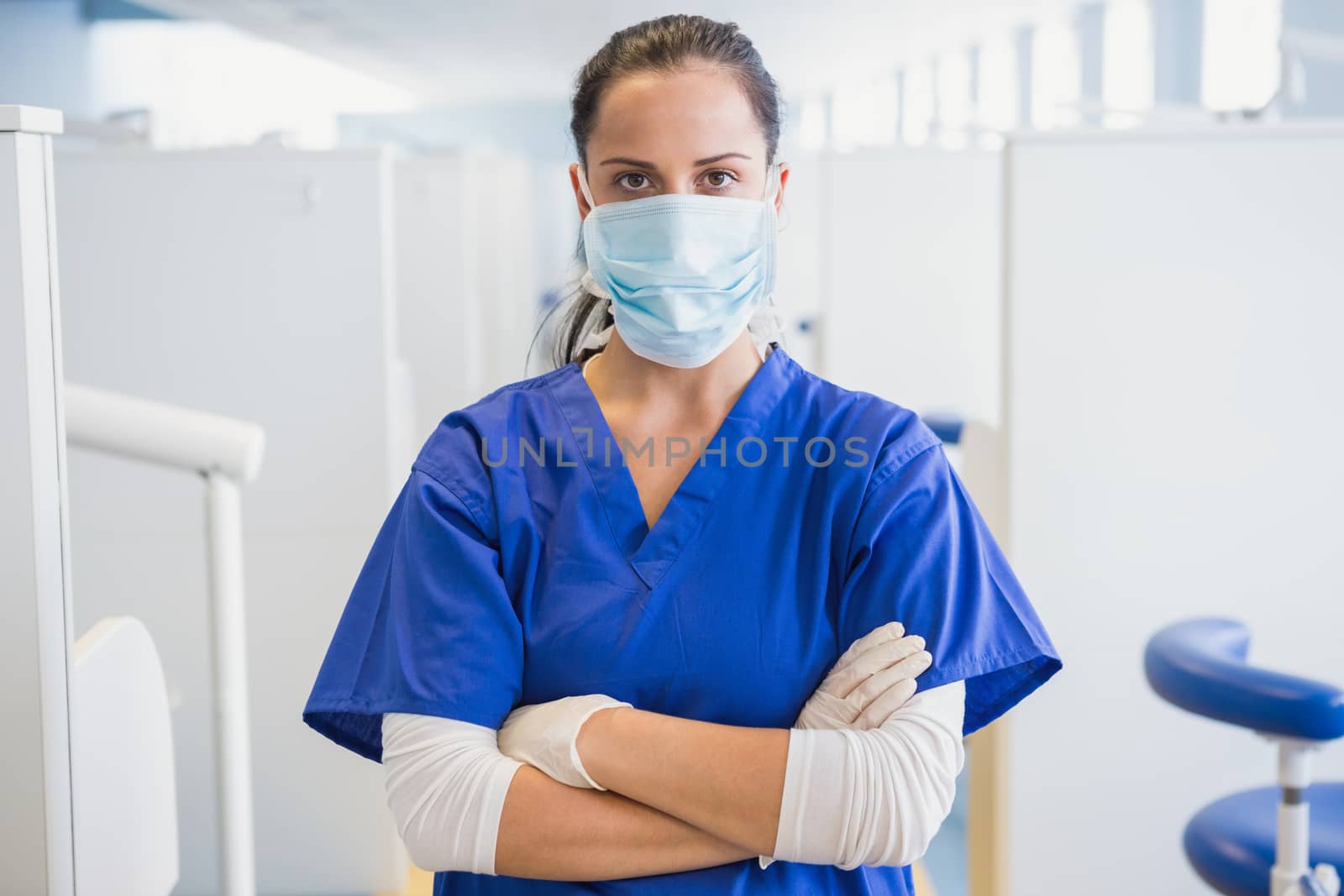 Dentist wearing surgical mask with arms folded in dental clinic
