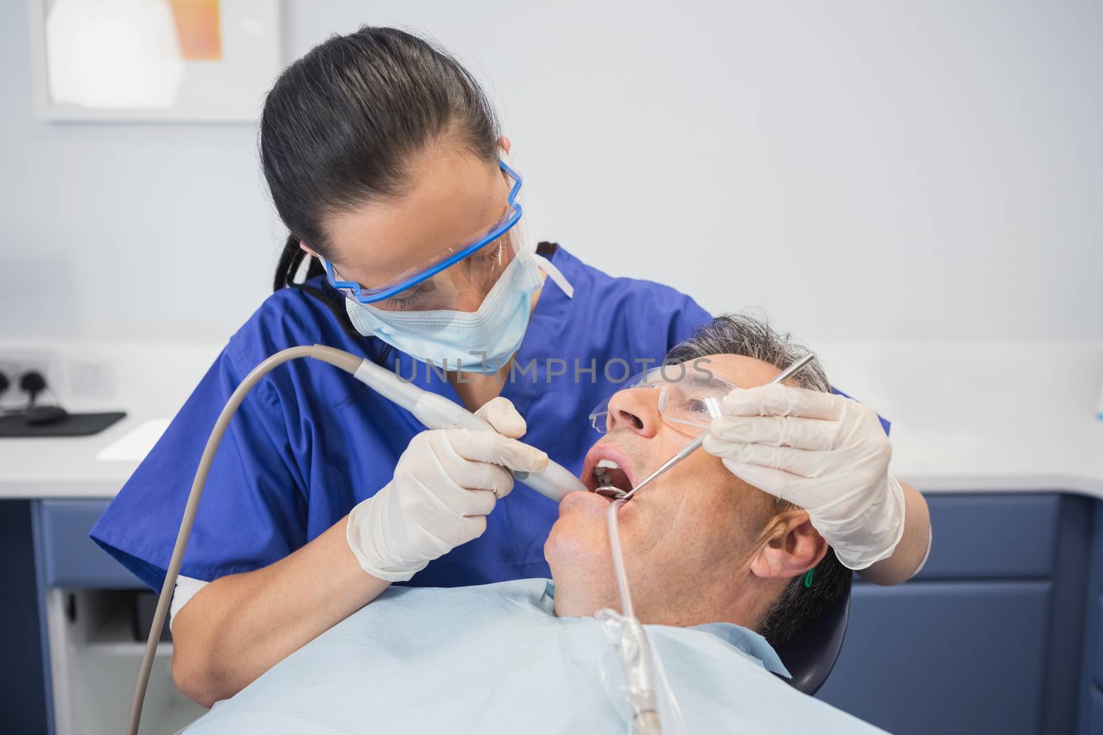 Dentist examining a patient with suction hose  by Wavebreakmedia