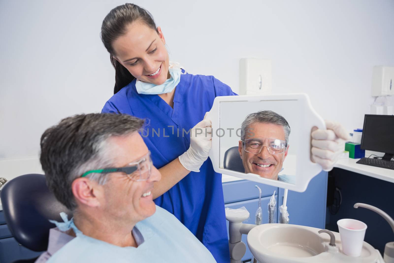 Smiling dentist showing teeth of her patient with a mirror by Wavebreakmedia