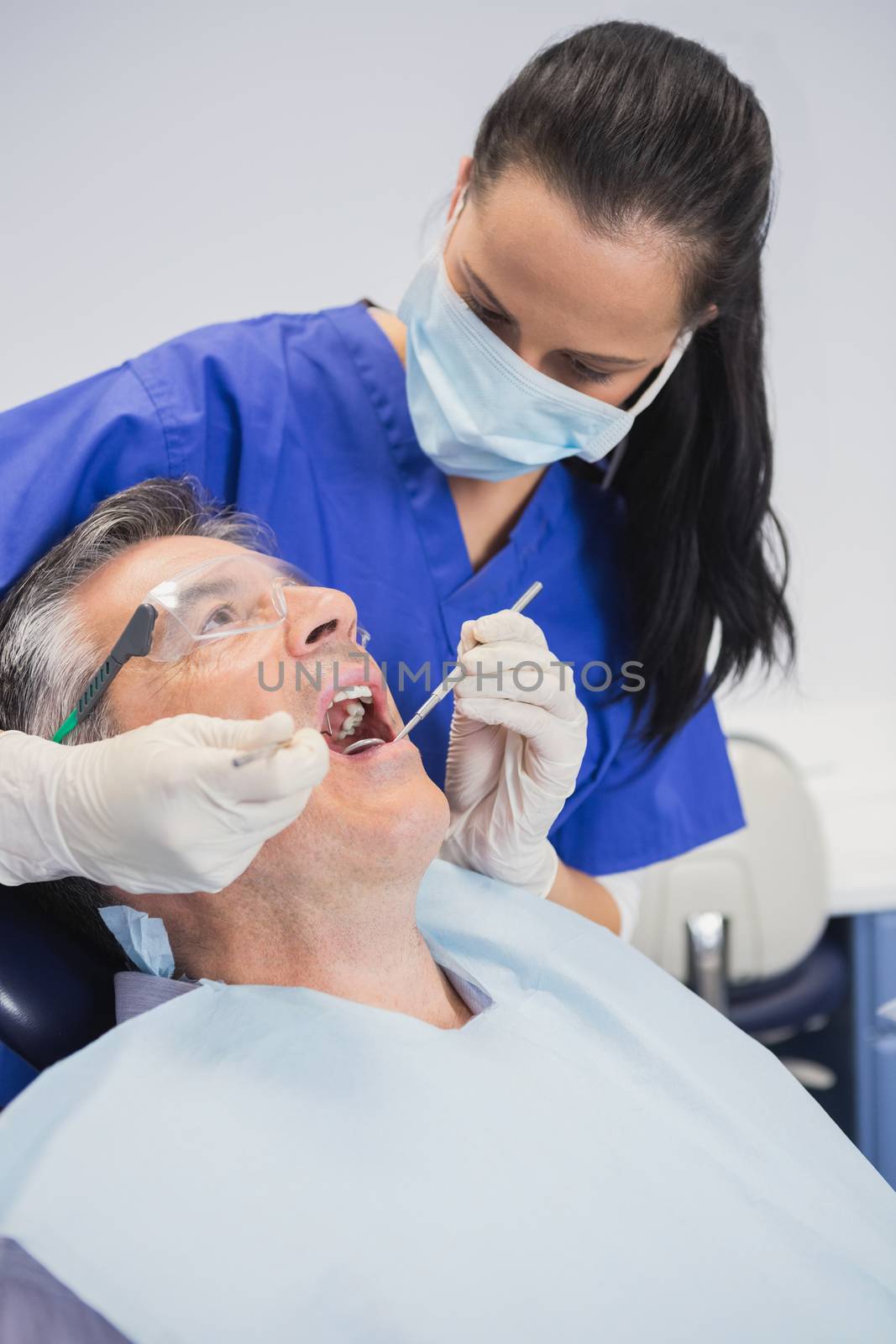 Dentist wearing surgical mask examining patient with tools