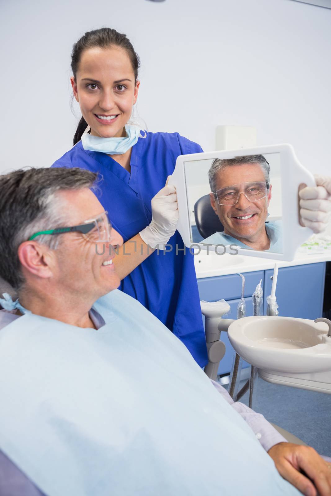 Smiling dentist showing teeth of her patient with a mirror in dental clinic