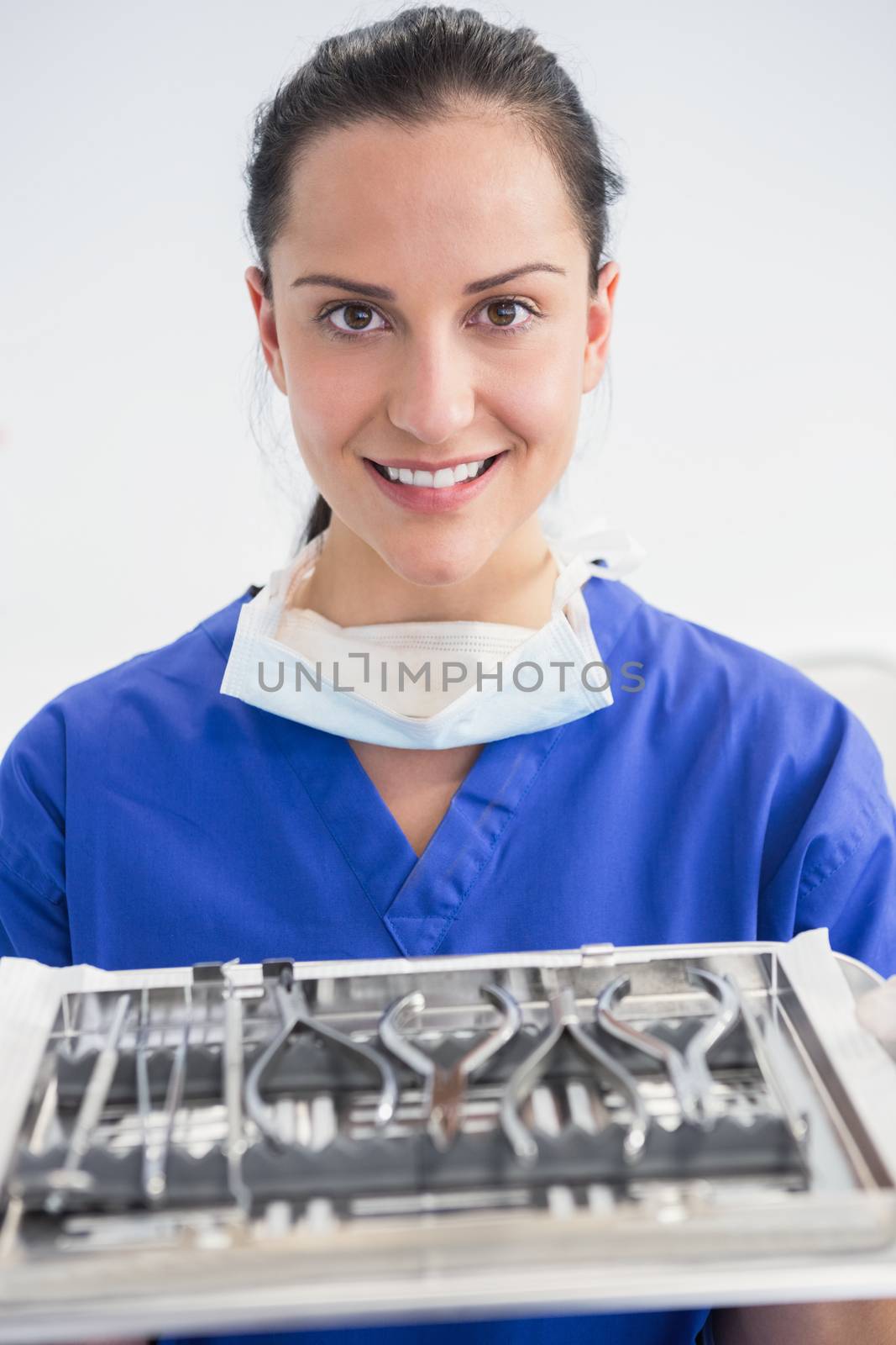 Smiling dentist holding tray with equipment in dental clinic