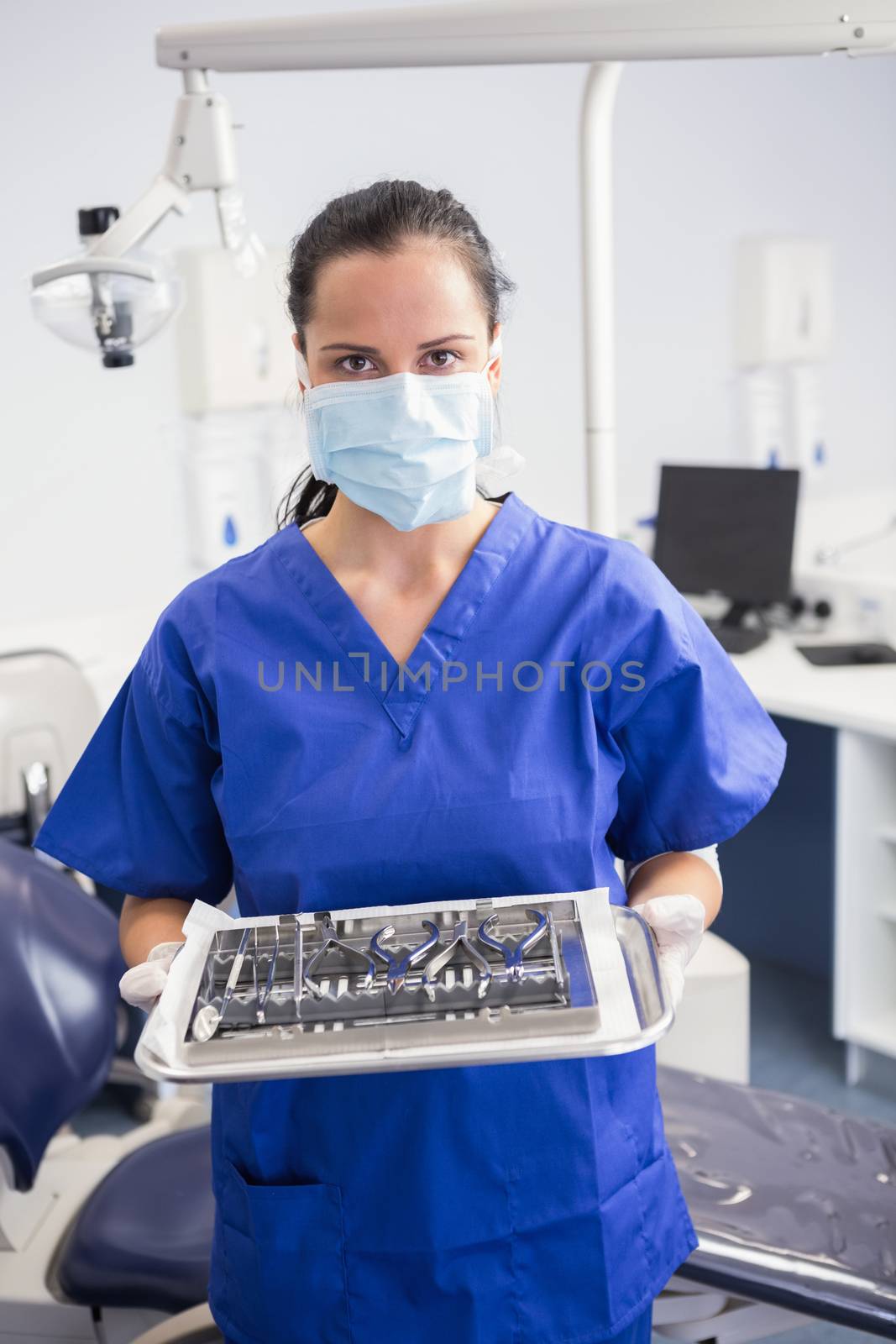 Portrait of a dentist with surgical mask and holding tray in dental clinic