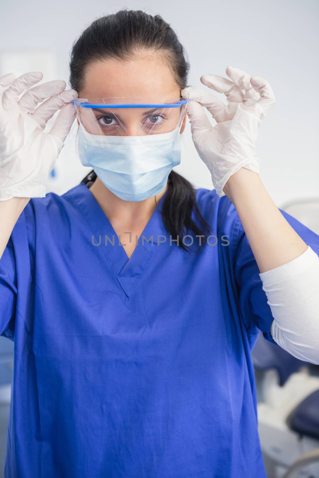 Dentist with surgical mask putting on her safety glasses in dental clinic 