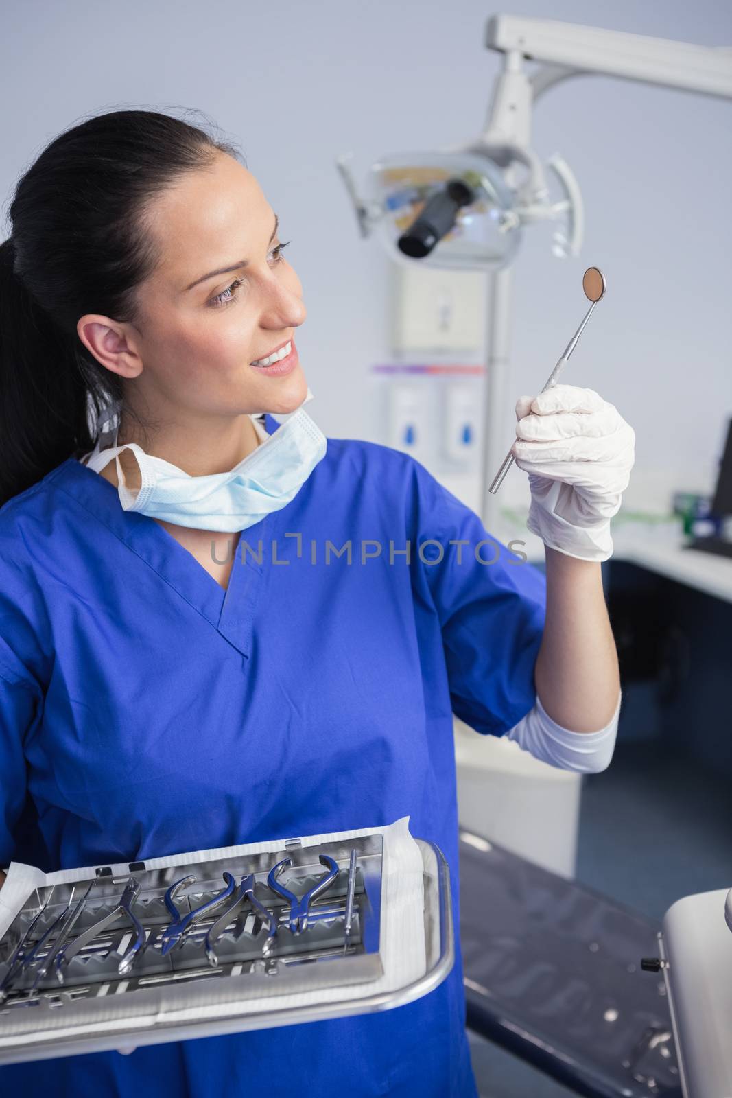 Smiling dentist holding tray and looking angle mirror  by Wavebreakmedia