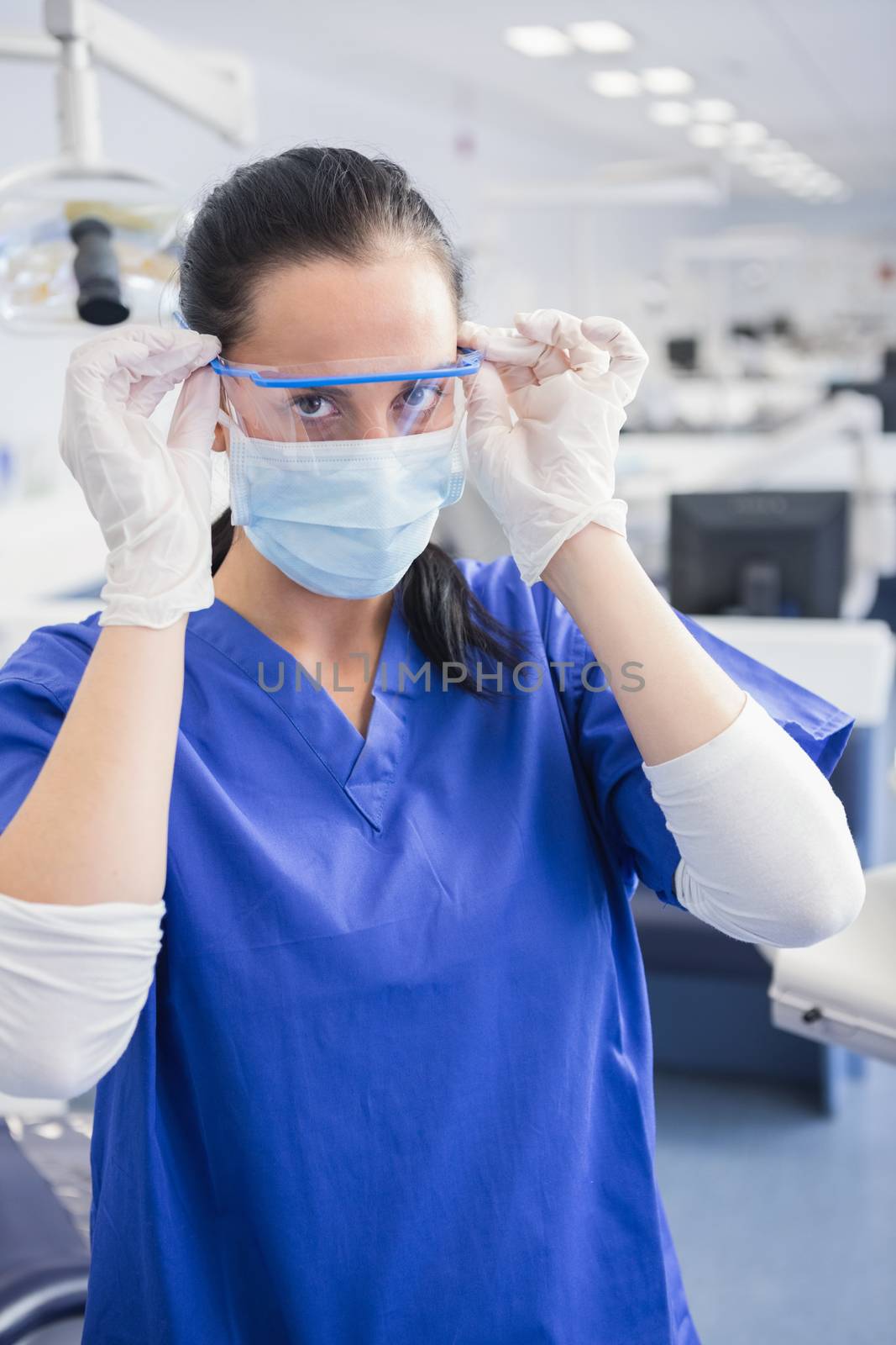 Dentist with surgical mask putting on her safety glasses in dental clinic 