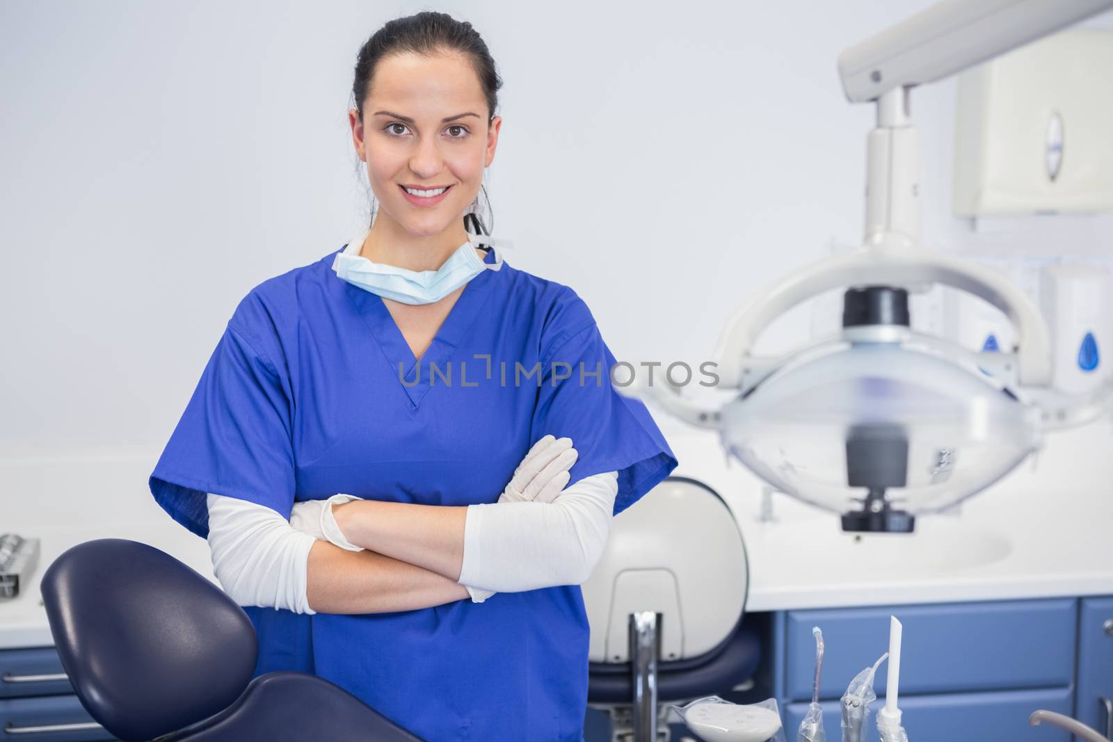 Portrait of a cheerful dentist with arms crossed behind dentists chair