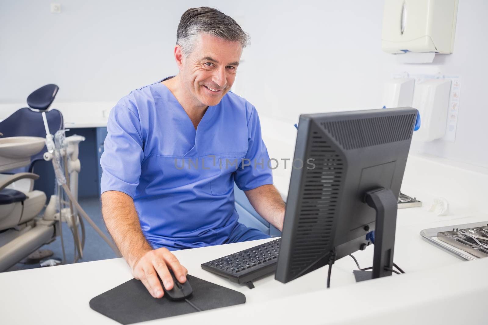 Portrait of a happy dentist using computer in dental clinic