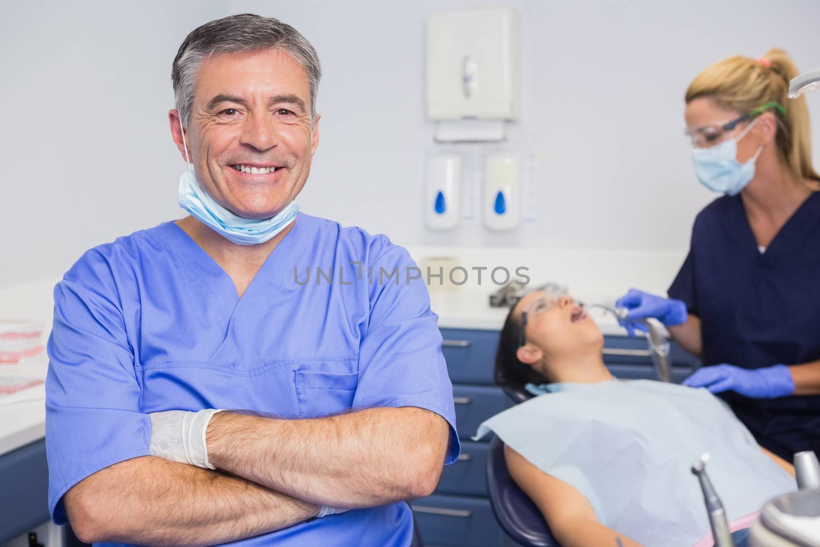 Portrait of a smiling dentist his arms crossed and his nurse with the patient behind him