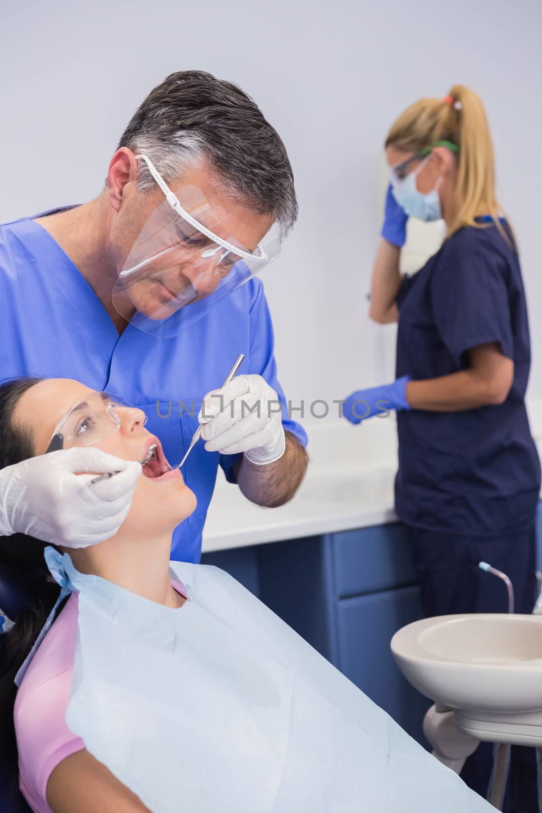 Dentist wearing face shield and examining a patient  by Wavebreakmedia