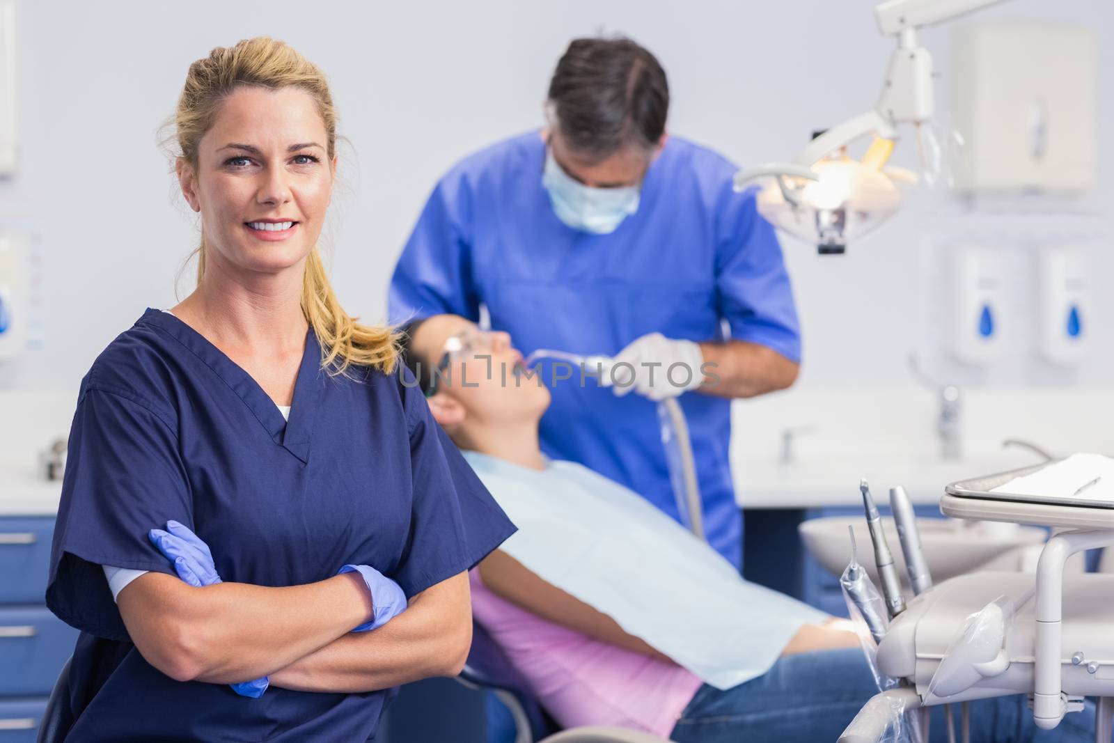 Portrait of a smiling nurse her arms crossed and dentist with the patient behind him