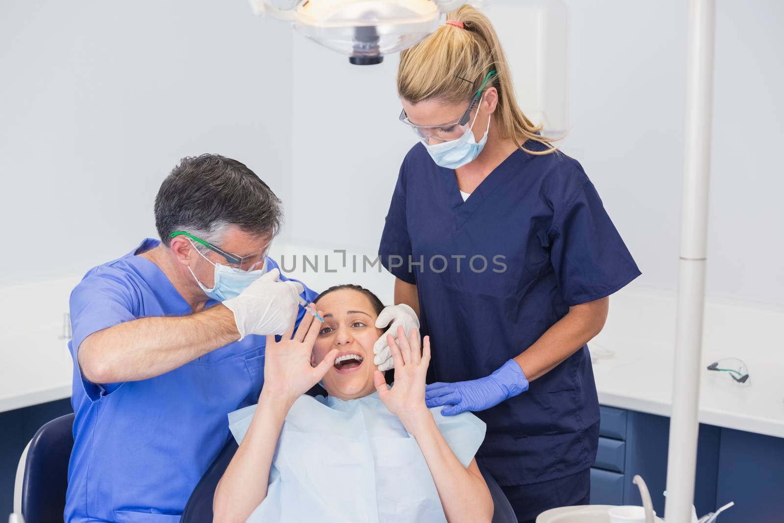 Dentist doing injection and patient protesting  by Wavebreakmedia