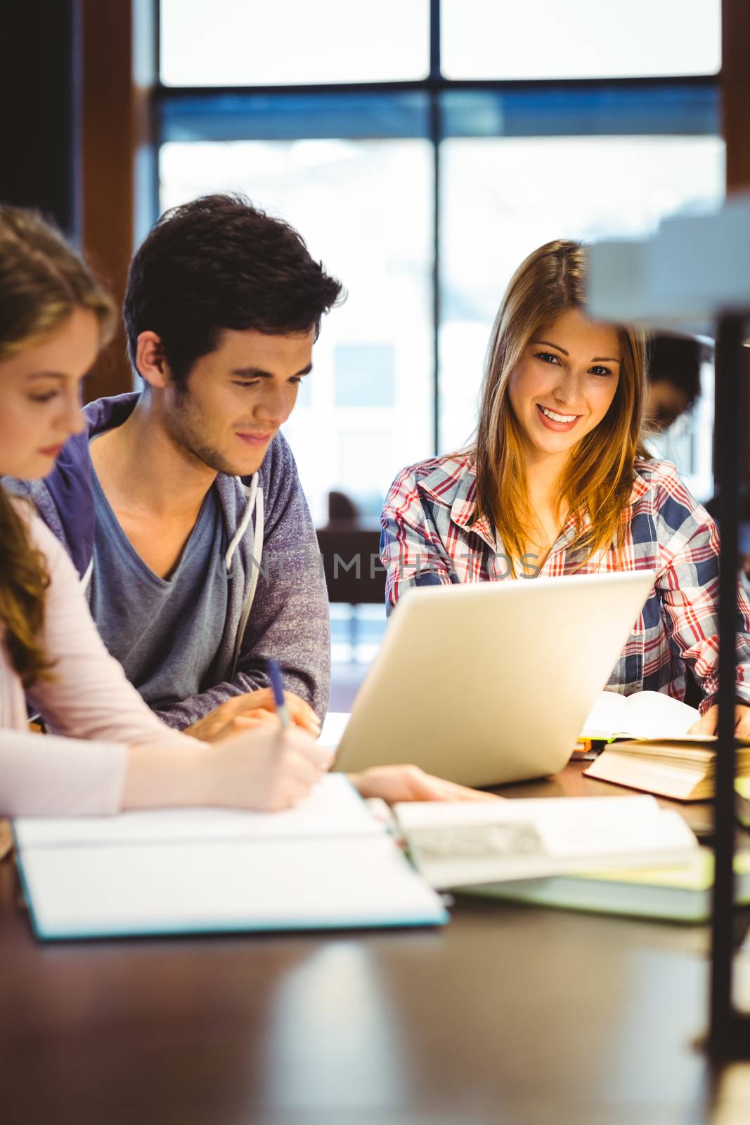 Student looking at camera while studying with classmates in library