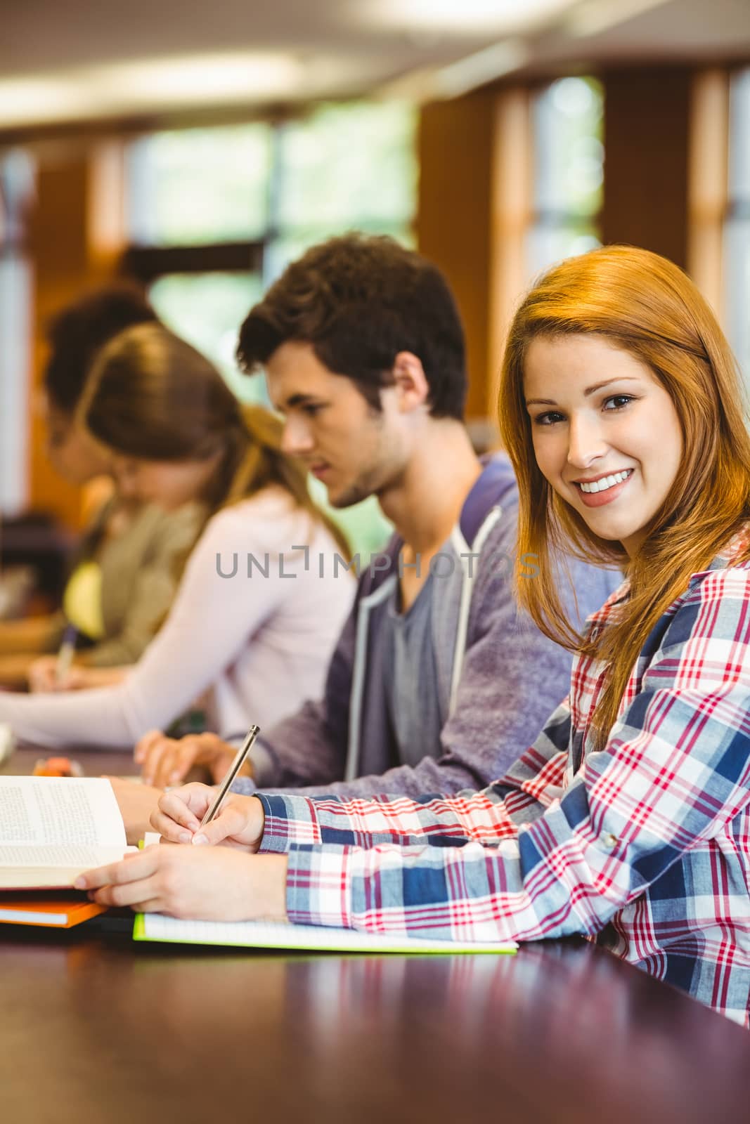 Student looking at camera while studying with classmates in library