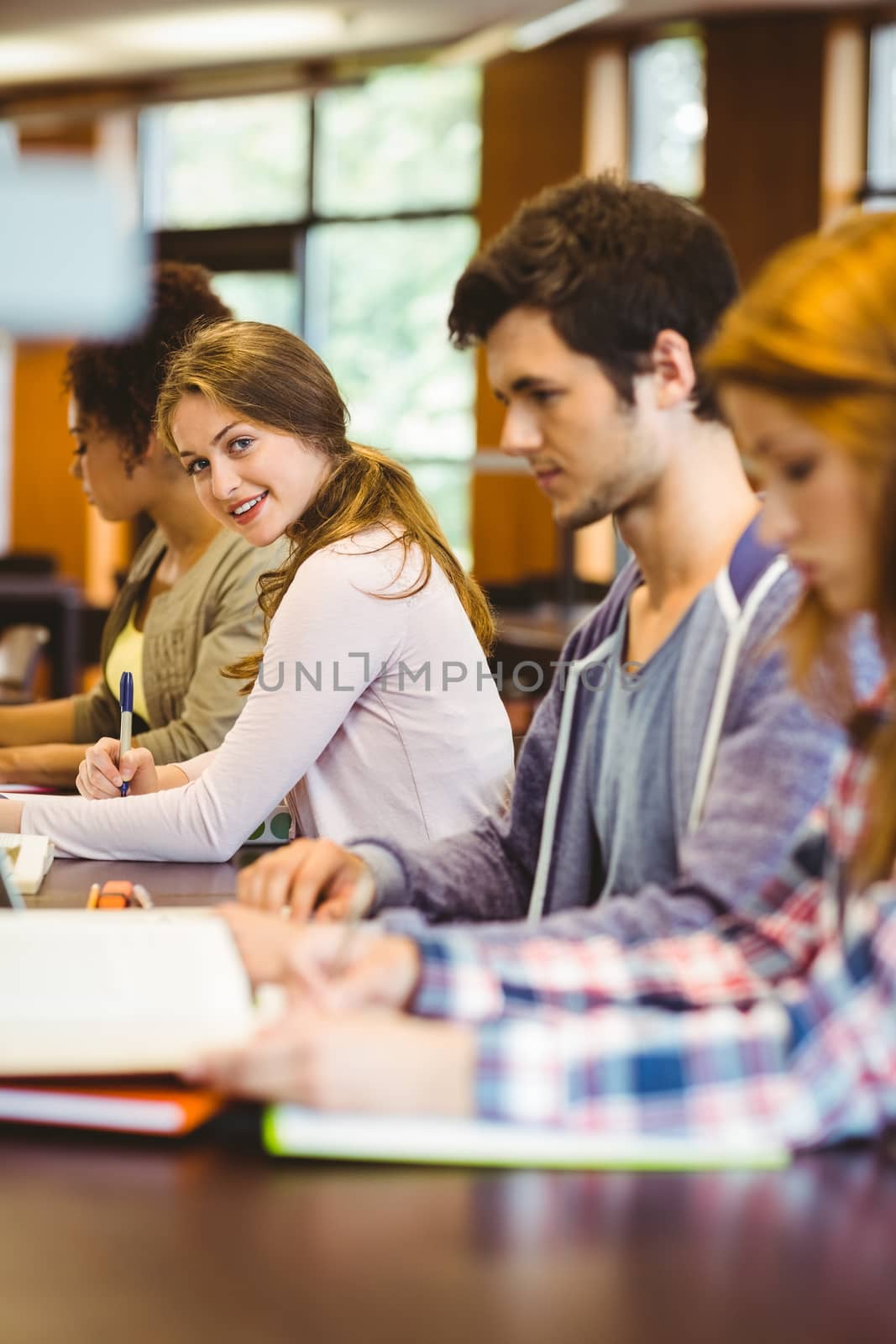 Student looking at camera while studying with classmates in library