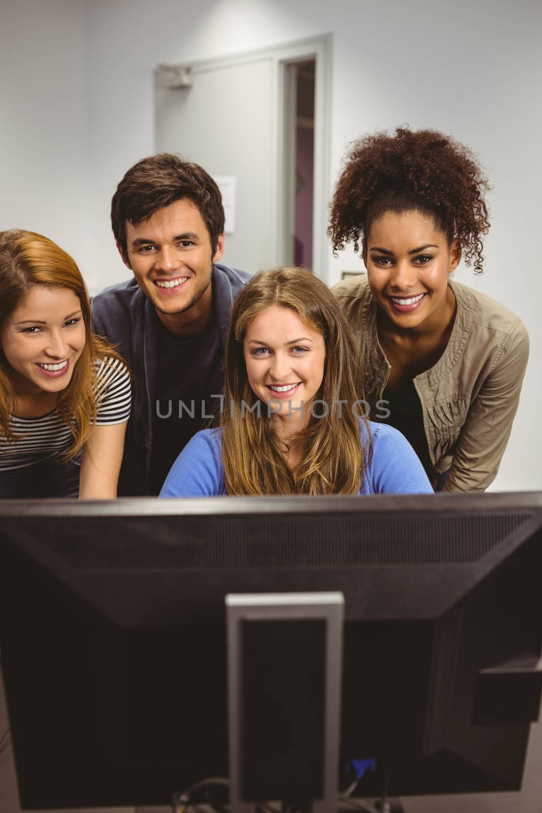 Smiling students using computer together looking at camera in classroom