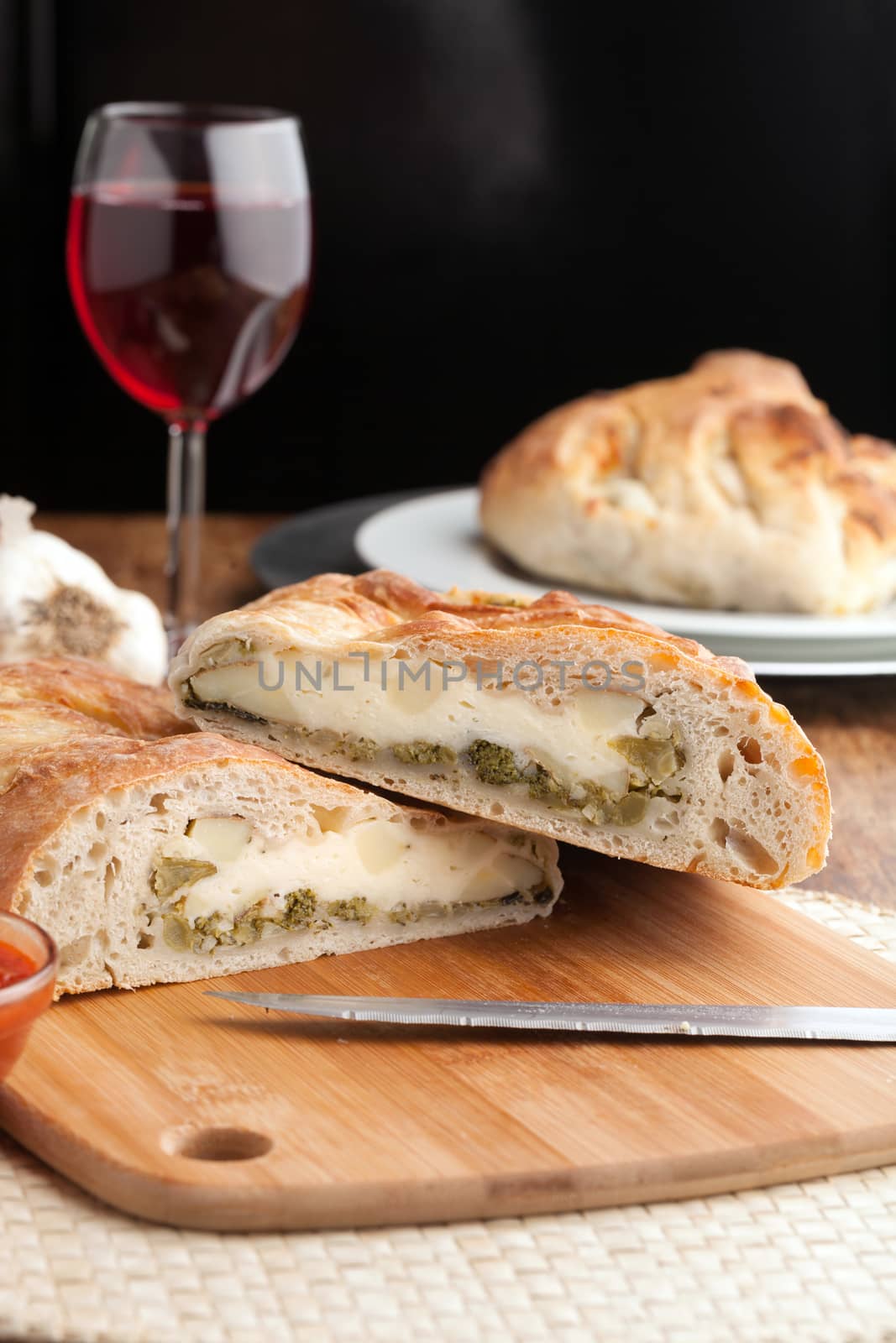 Homemade stromboli or stuffed bread with broccoli potatoes garlic onions and mozzarella cheese along with a side of marinara dipping sauce.