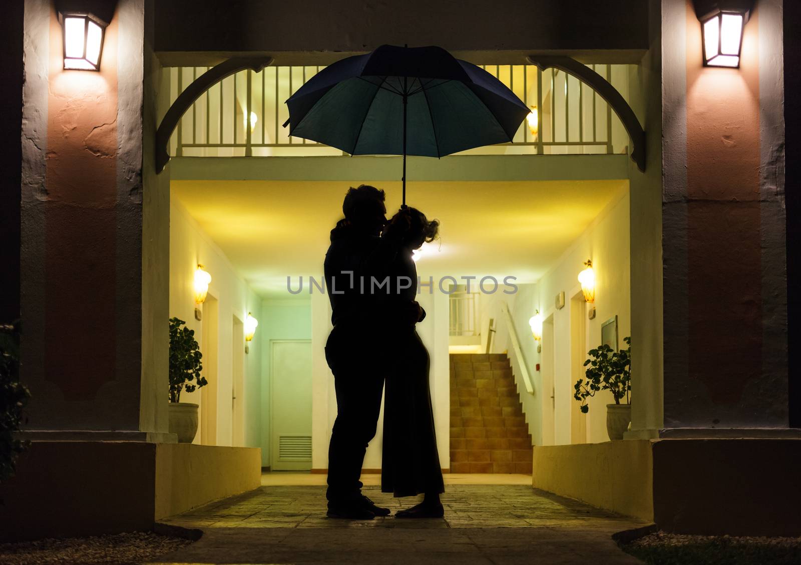 Couple in silhouette Kissing Under Umbrella In Front of Apartment Entrance