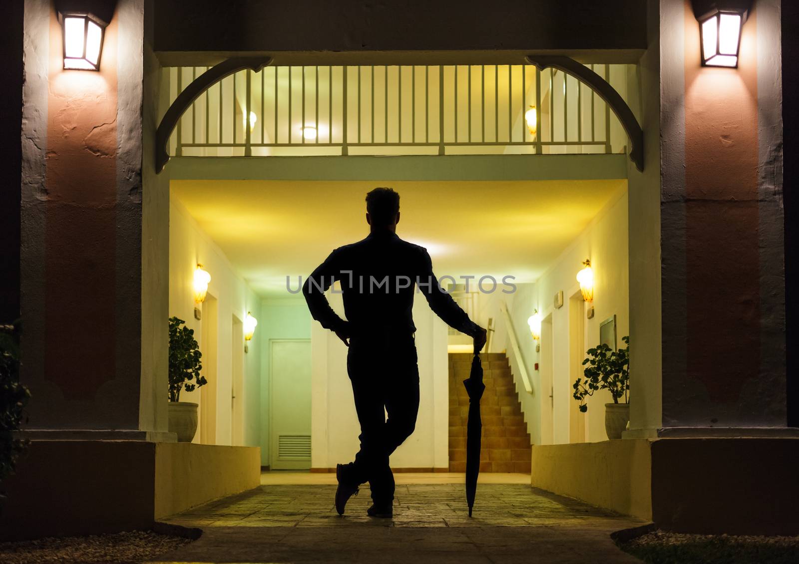 Man in Silhouette with Umbrella Standing up In Front of Apartment Entrance