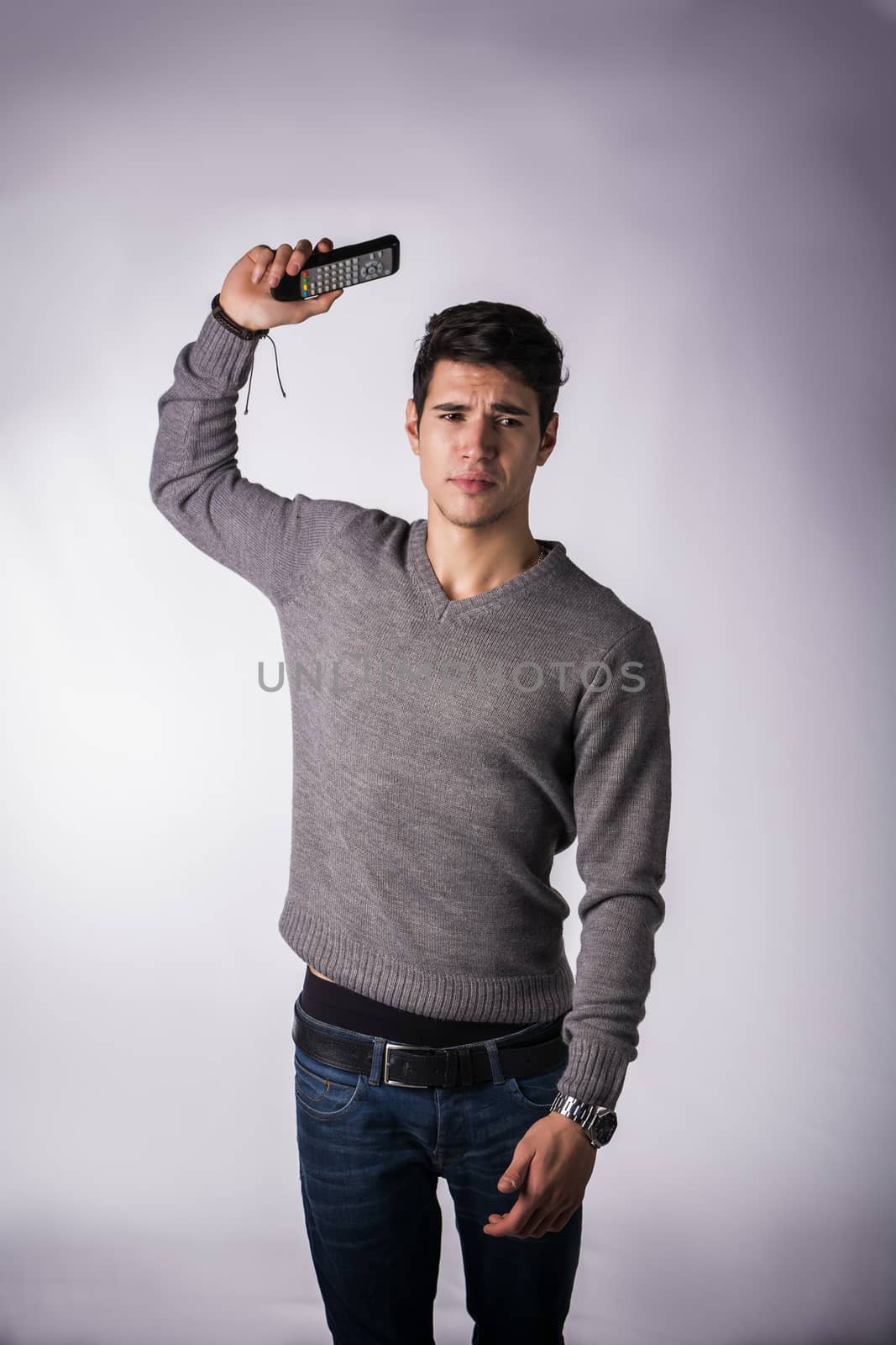 Attractive young man throwing away remote control with disgusted expression, standing on white