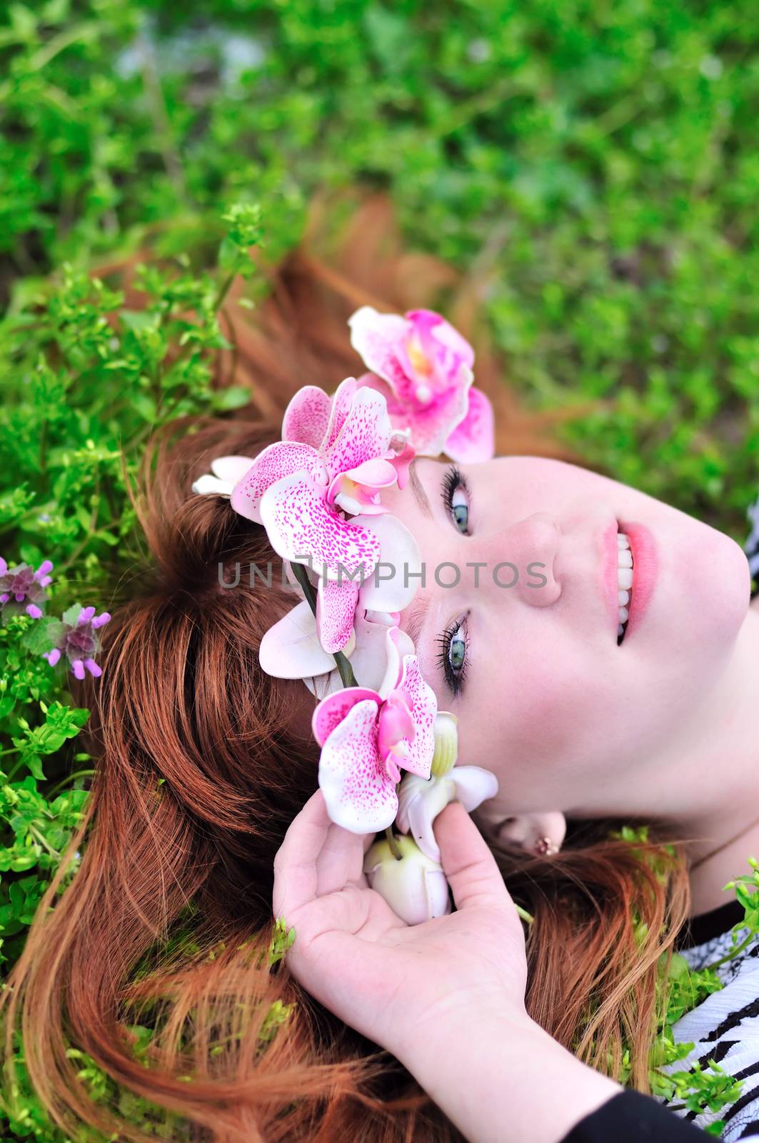Portrait of the beautiful redheaded girl with orchid on the meadow