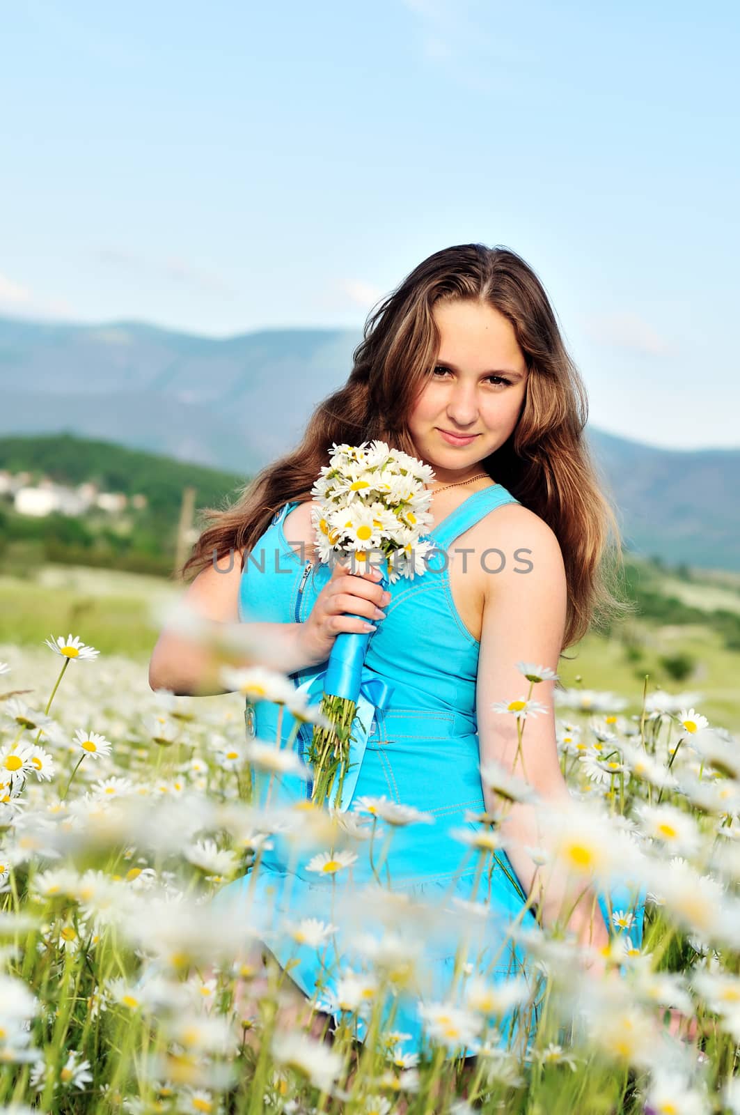 teen girl sitting in daisy field and holding bunch of flowers 