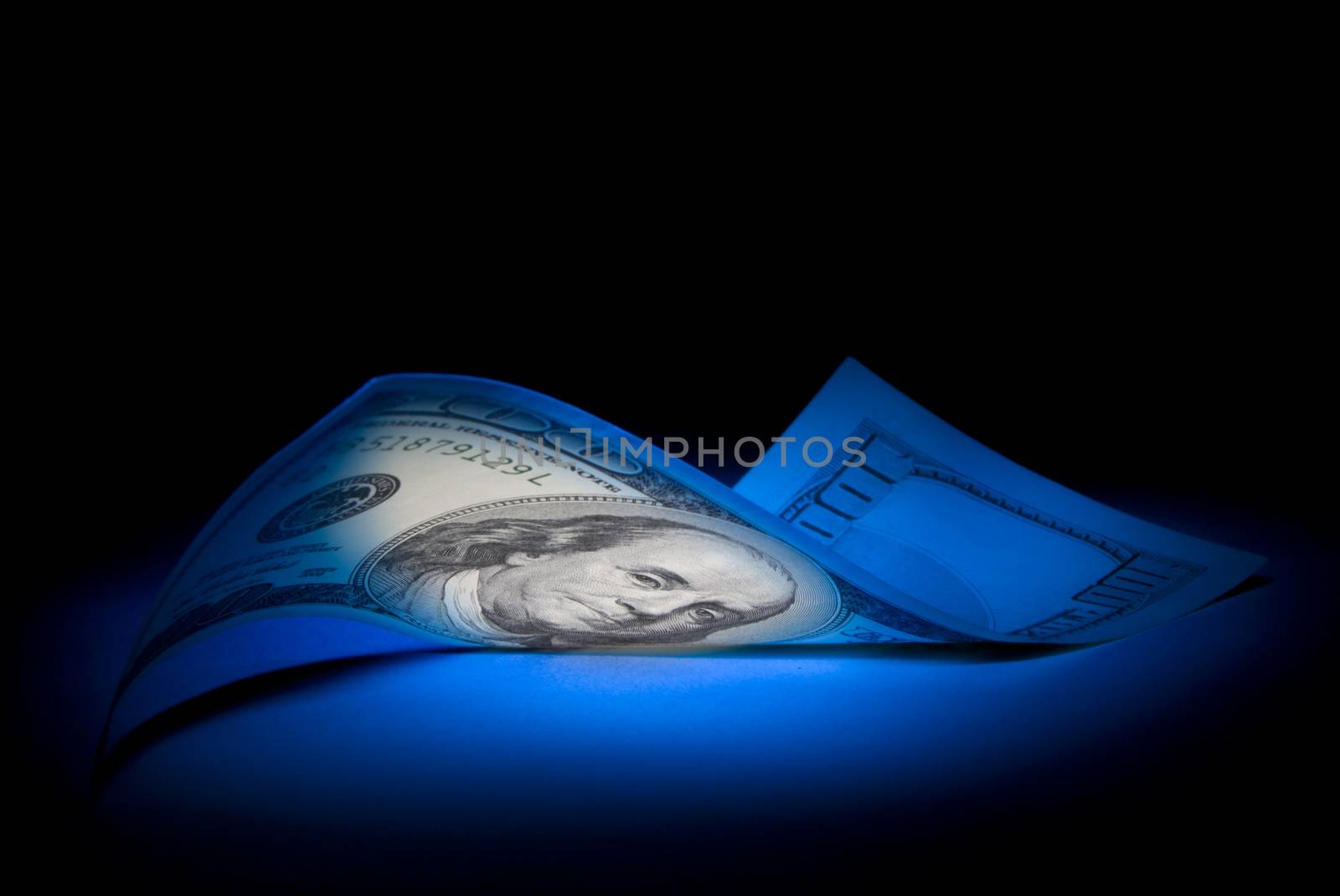 Hundred dollars. Dark blue art illumination.
Black background. 