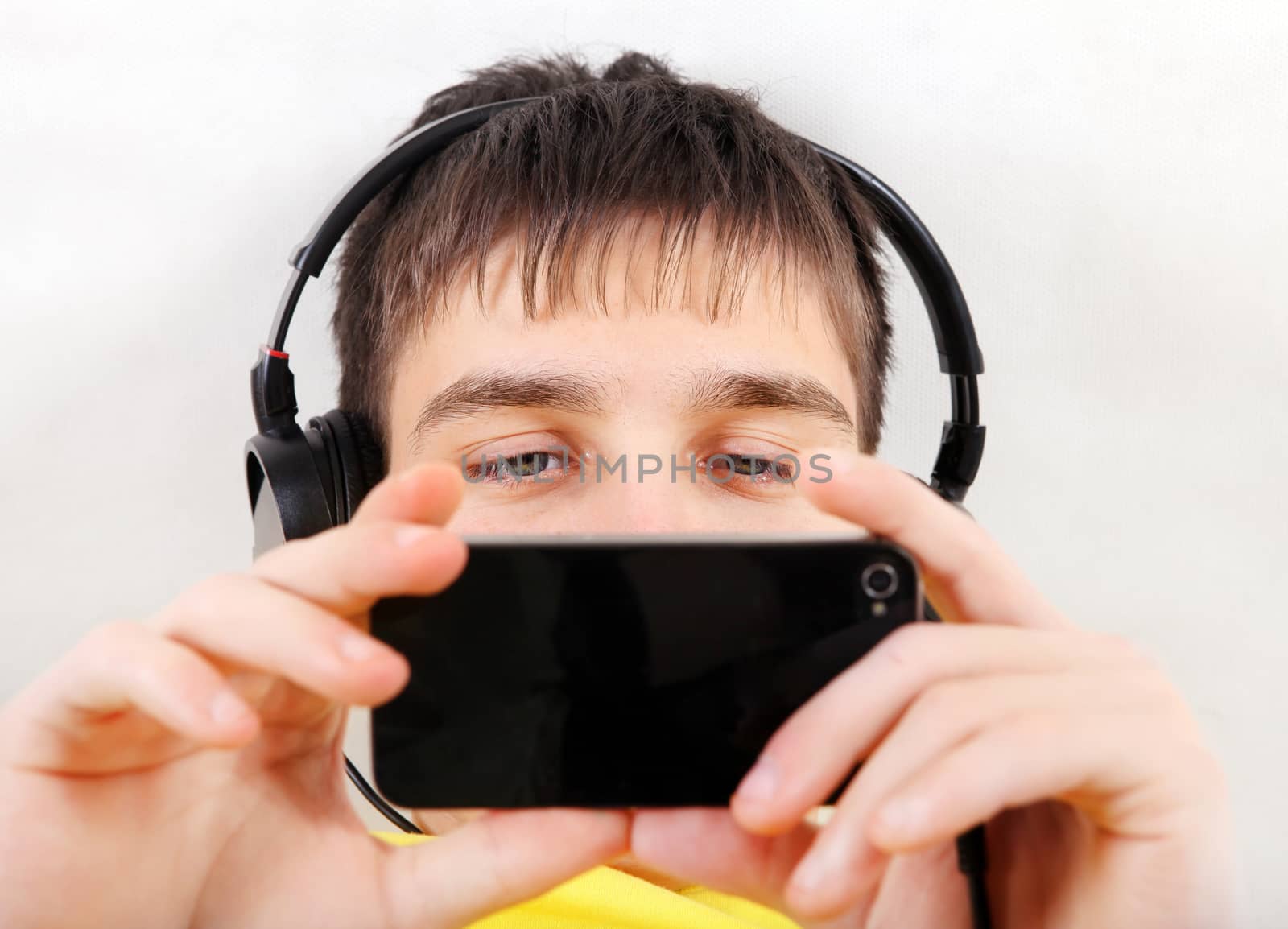 Teenager in Earphones with Cellphone on the White Wall Background closeup