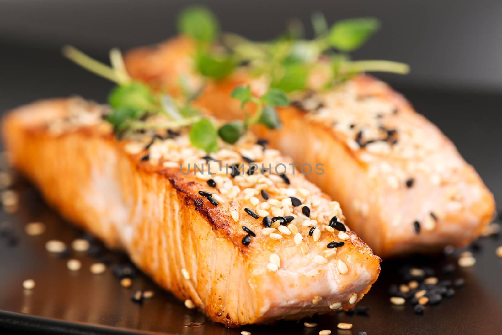 Grilled salmon, sesame seeds  and marjoram on a black plate. Studio shot