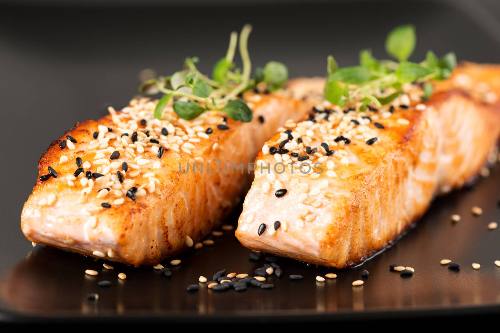 Grilled salmon, sesame seeds  and marjoram on a black plate. Studio shot