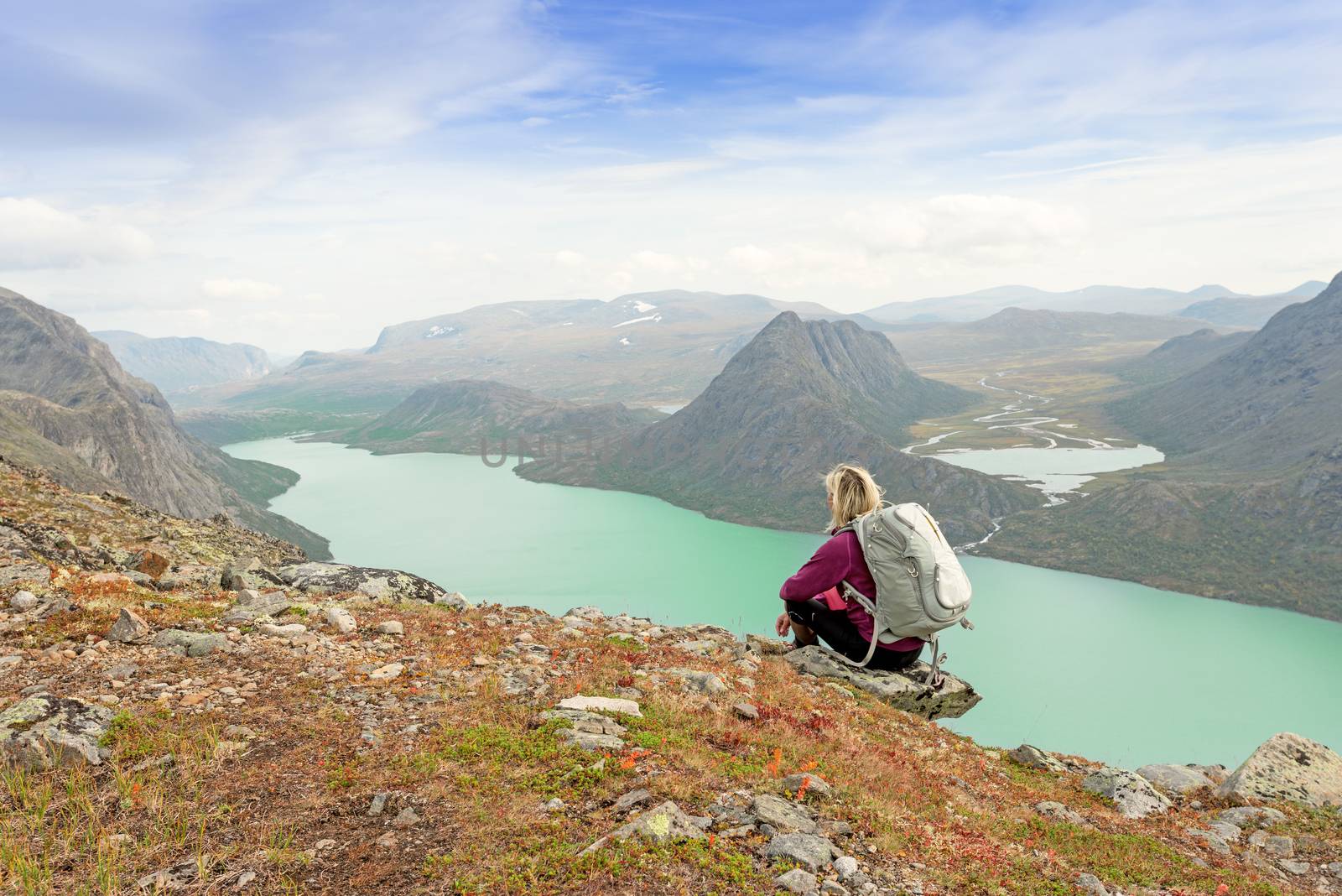 Hiker with backpack relaxing on cliff of a mountain and enjoying valley and lake view at Jotunheimen National Park, Norway