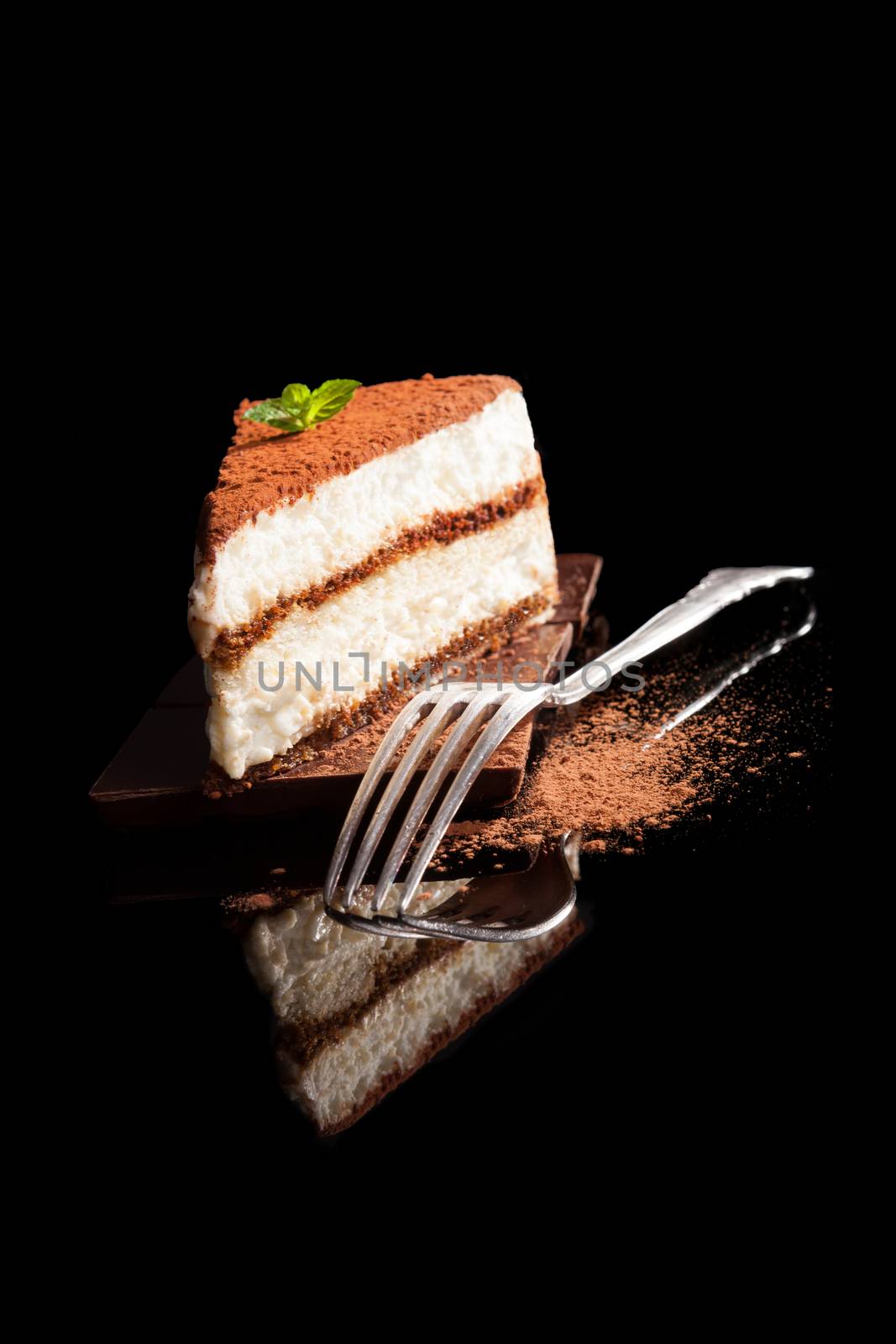 Tiramisu dessert on chocolate bar isolated on black background with silver fork. Italian sweet dessert concept.