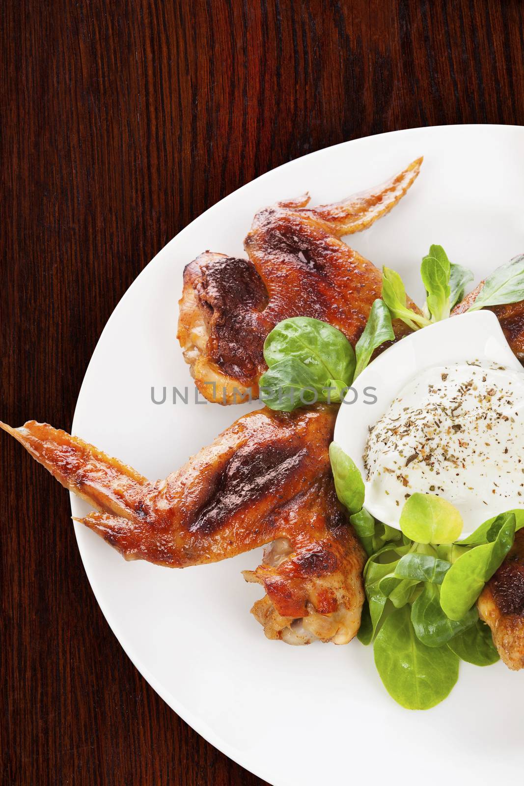 Delicious buffalo wings with fresh salad on brown wooden background. Culinary eating. 
