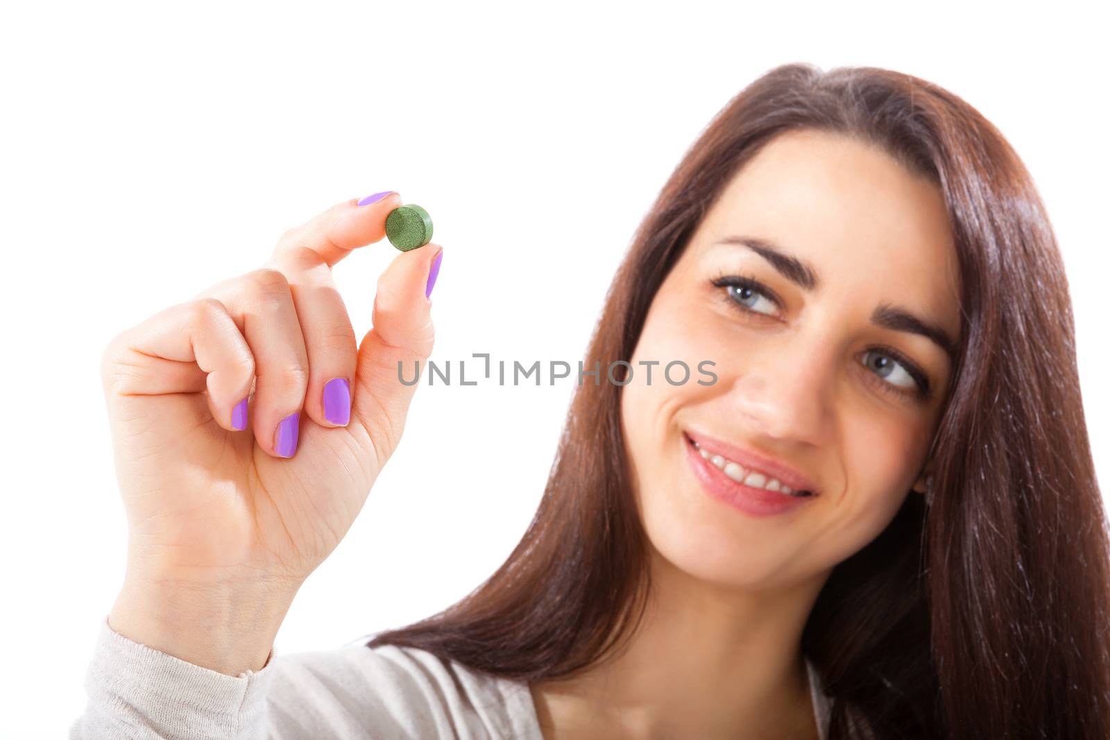 Beautiful smiling girl in her 20s holding green chlorella and spirulina pill isolated on white background. Healthy eating, green superfood.