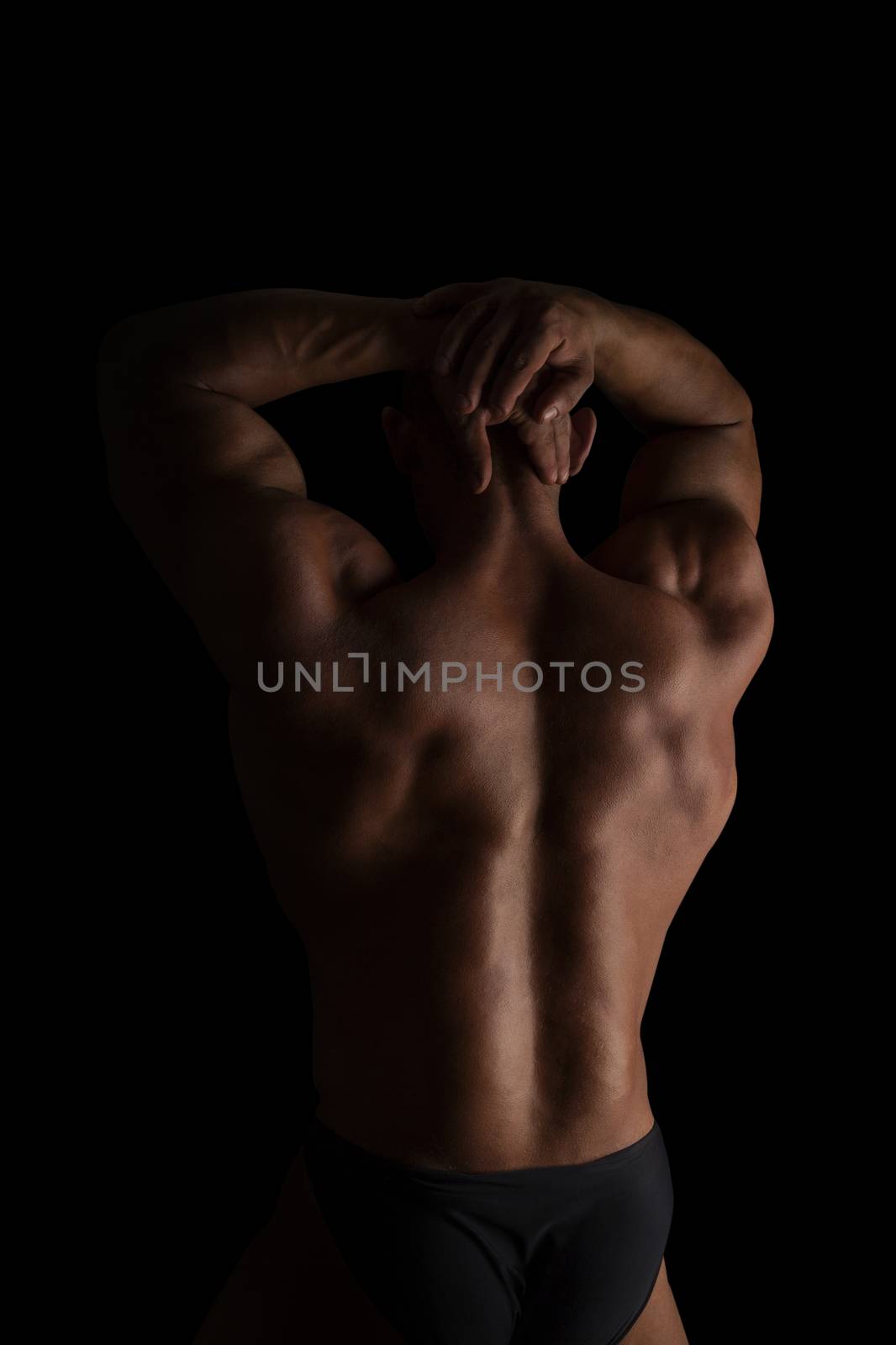 Handsome shirtless bodybuilder showing huge back isolated on black background. Sports and fitness.