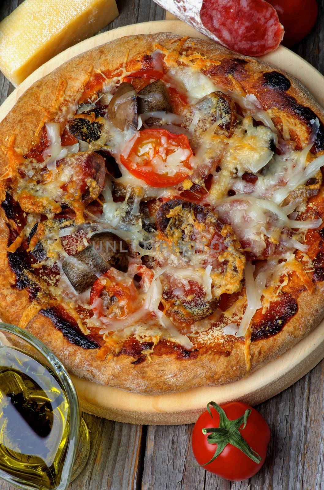 Homemade Pizza with Edible Mushrooms, Tomatoes, Salami and Grated Cheese on Circle Cutting Board and Ingredients on Wooden background. Top View