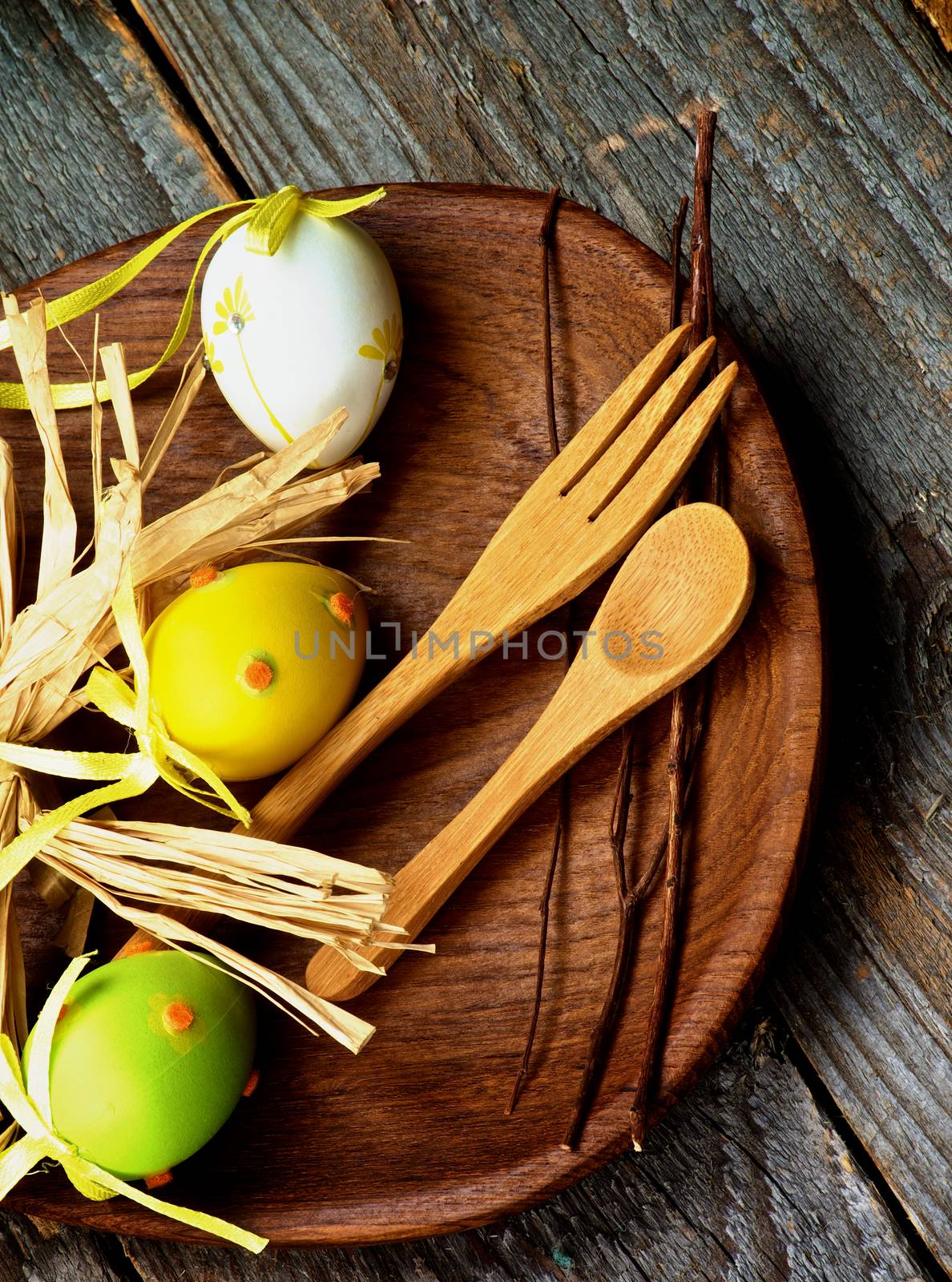 Easter Table Setting with Colored Eggs, Wooden Fork and Spoon, Natural Branches on Wooden Plate closeup on Rustic Wooden background