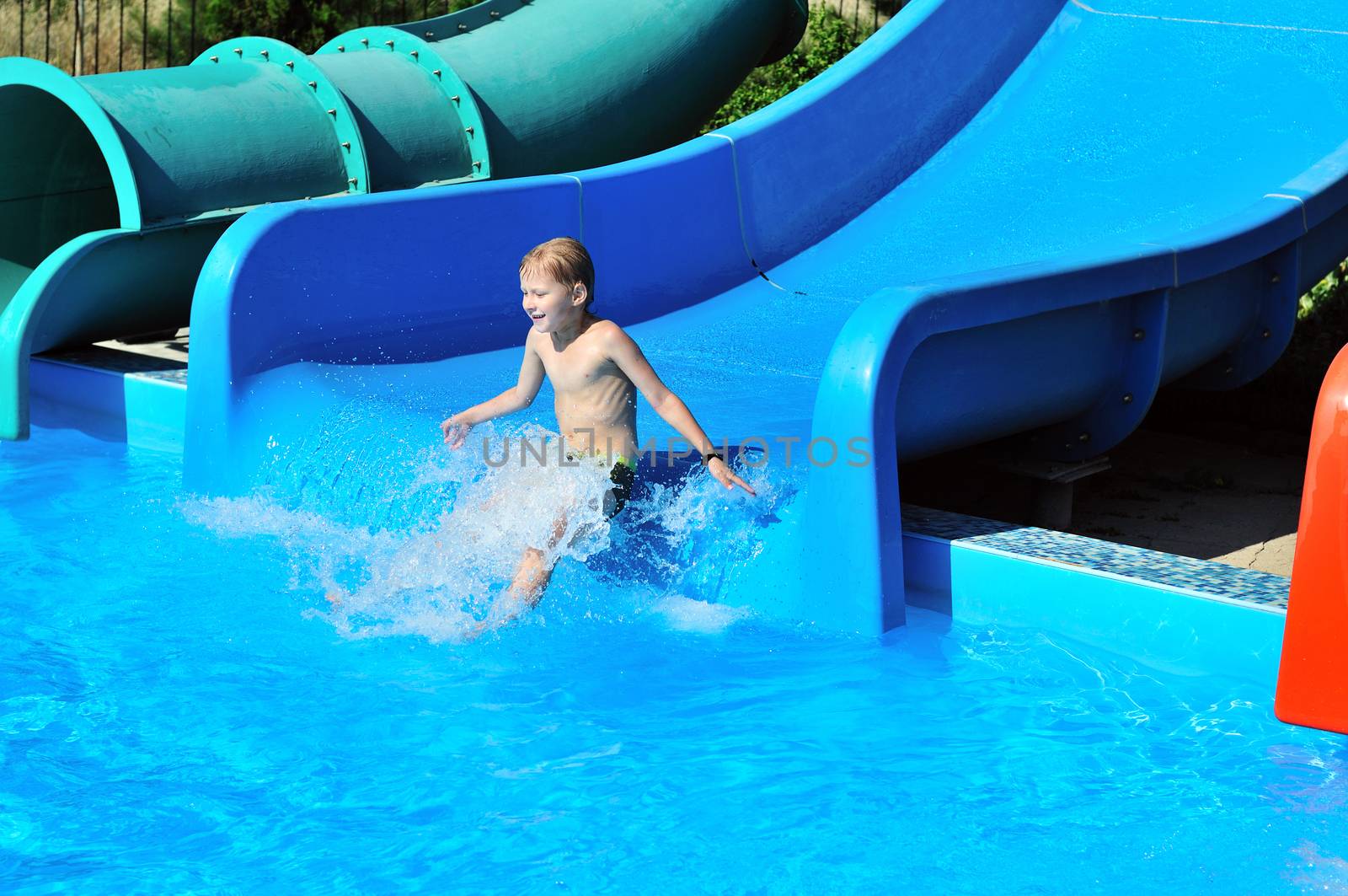 Cute little boy sliding down a water slide to pool
